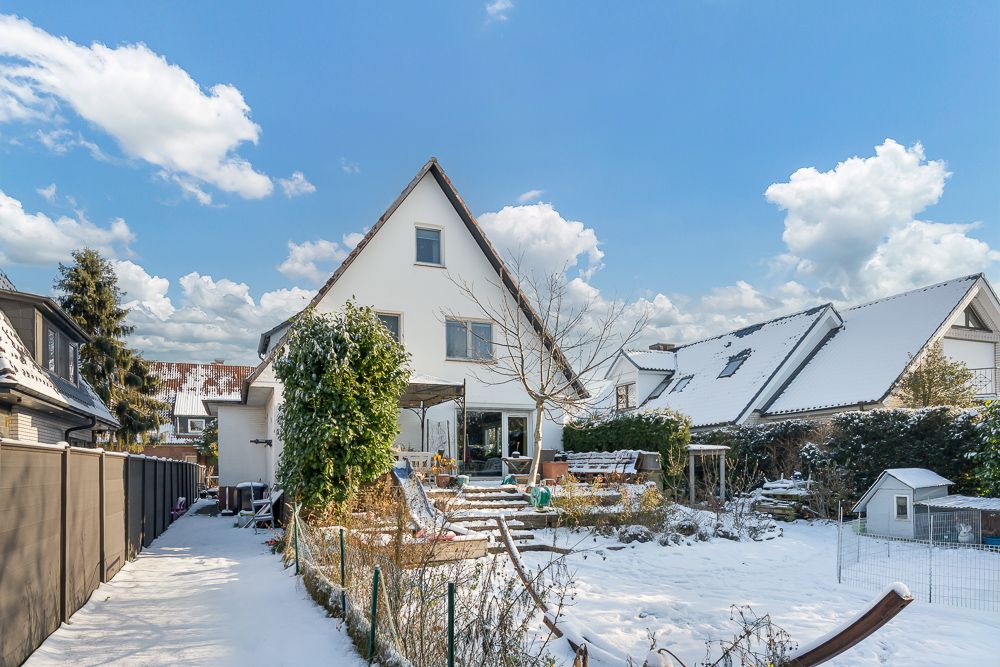Schneebedecktes Einfamilienhaus mit Garten und Terrasse an einem sonnigen Tag.