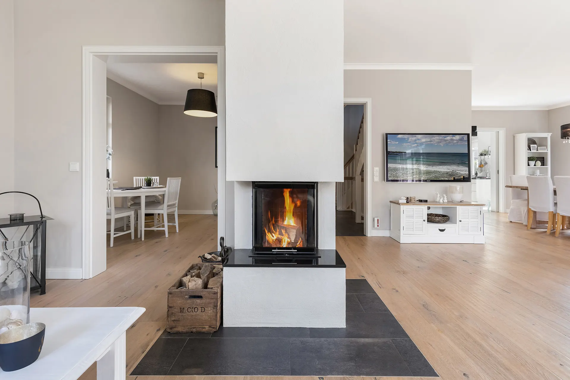 Modernes Wohnzimmer mit Kamin, Fernseher und Essbereich, heller Holzboden.