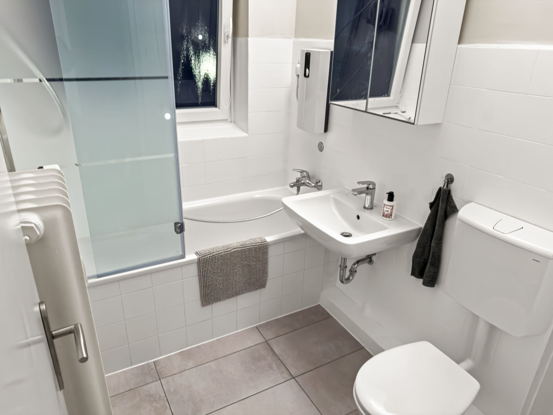 Modernes Bad mit Badewanne, Waschbecken, Spiegel, WC und Handtüchern, Fliesenboden.