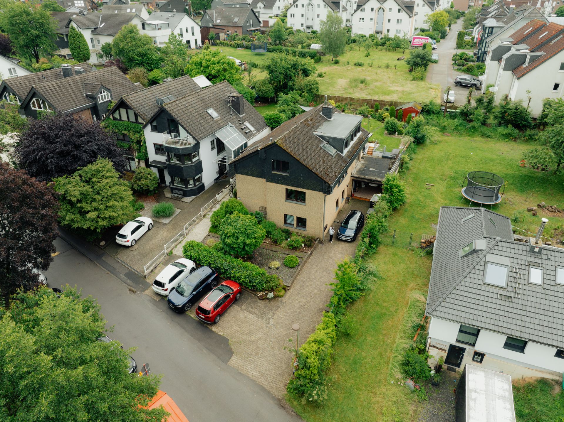 Luftaufnahme von Wohnhäusern mit Gärten und parkenden Autos in einer grünen Nachbarschaft.