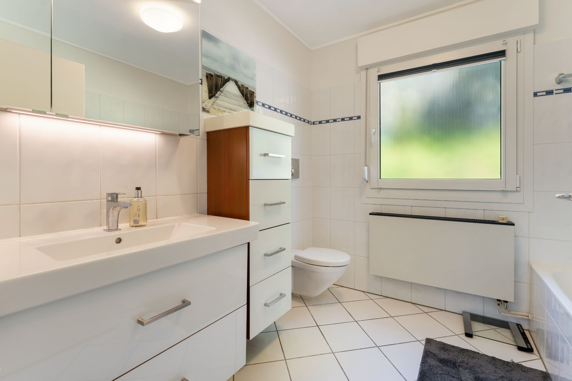 Modernes Badezimmer mit Waschbecken, Schrank, Toilette und Fenster.