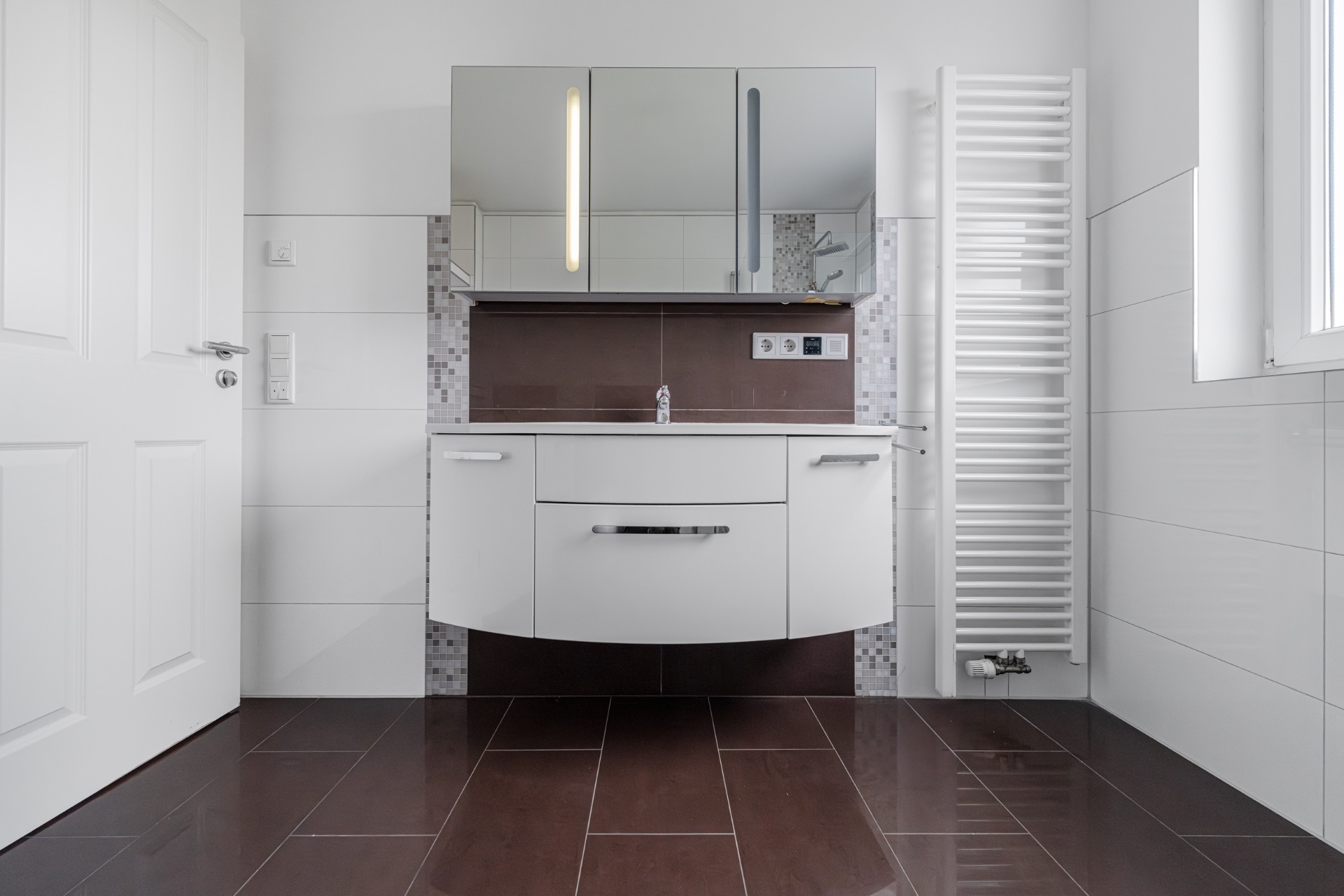 Modernes Badezimmer mit Waschbecken, Spiegelschrank und Handtuchheizkörper.