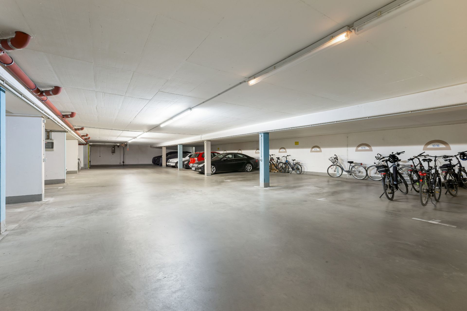 Helle Tiefgarage mit geparkten Autos und Fahrrädern auf der rechten Seite.