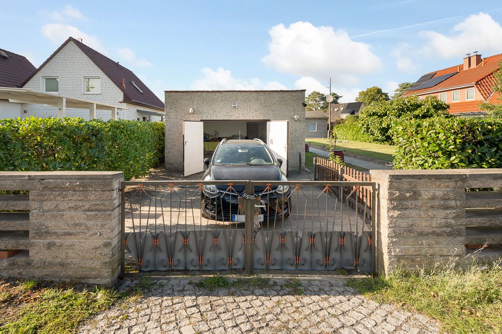 Auto steht vor einer offenen Garage hinter einem Metalltor mit Steinmauern links und rechts.