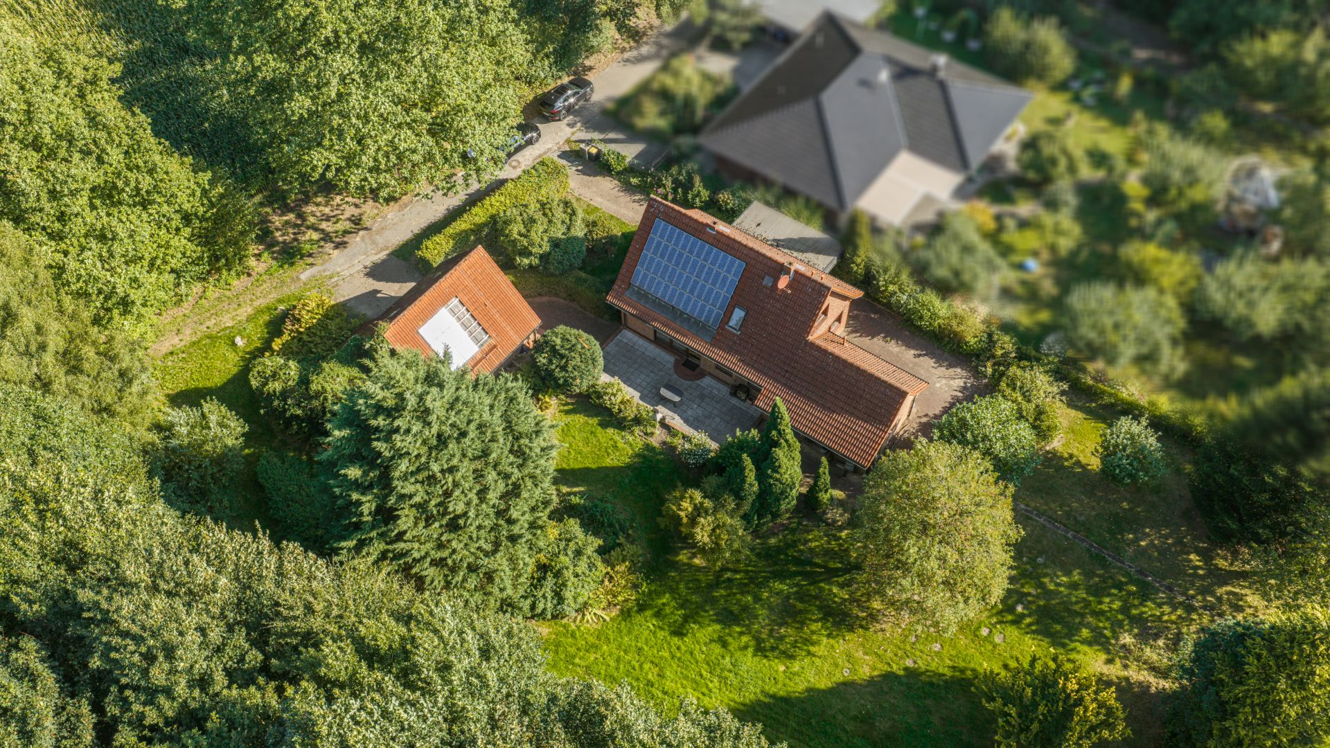 Luftaufnahme eines Hauses mit Solarpanelen und Garten, umgeben von Bäumen.