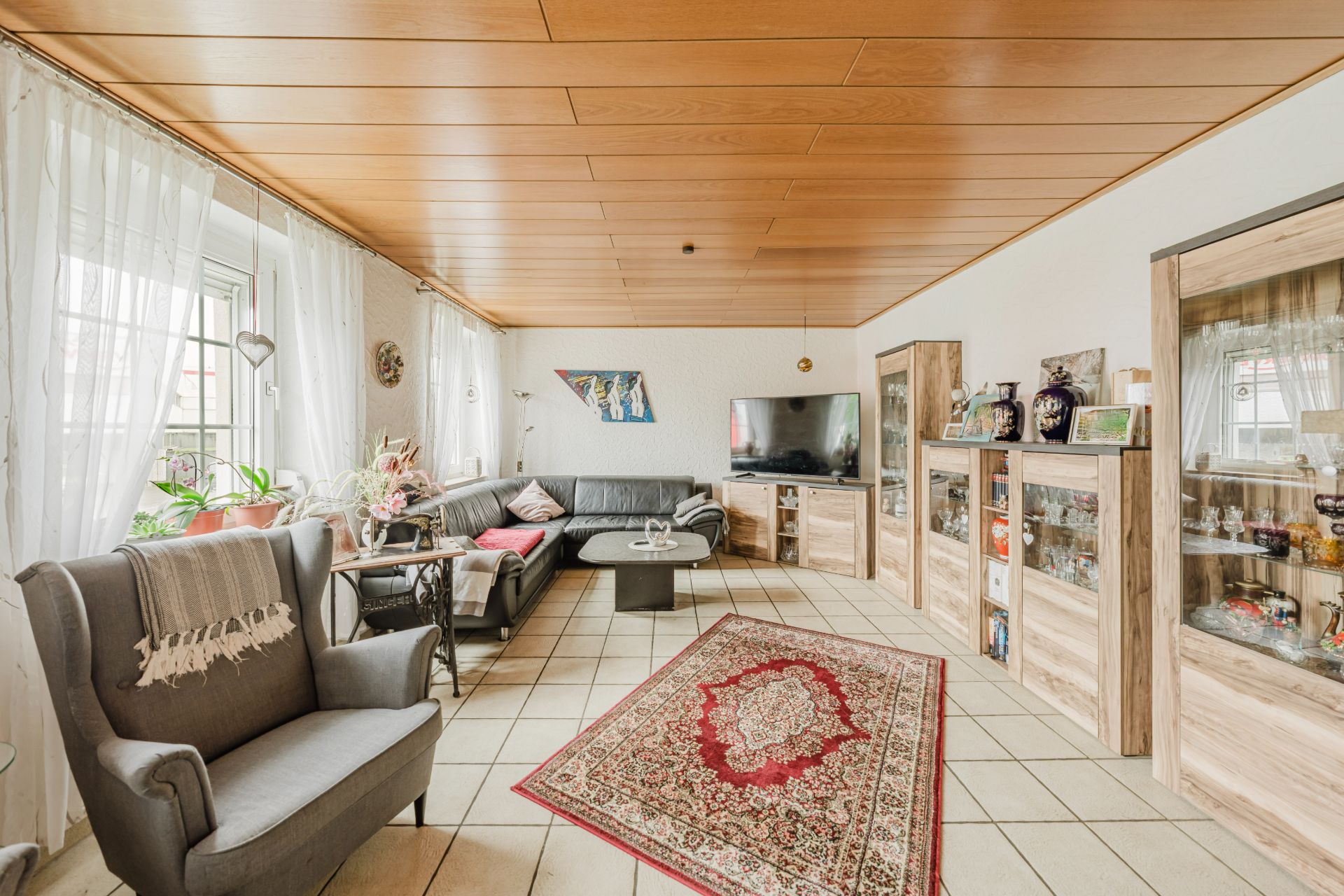 Helles Wohnzimmer mit Sofa, Sessel, Teppich, Schrankwand und Fernseher.