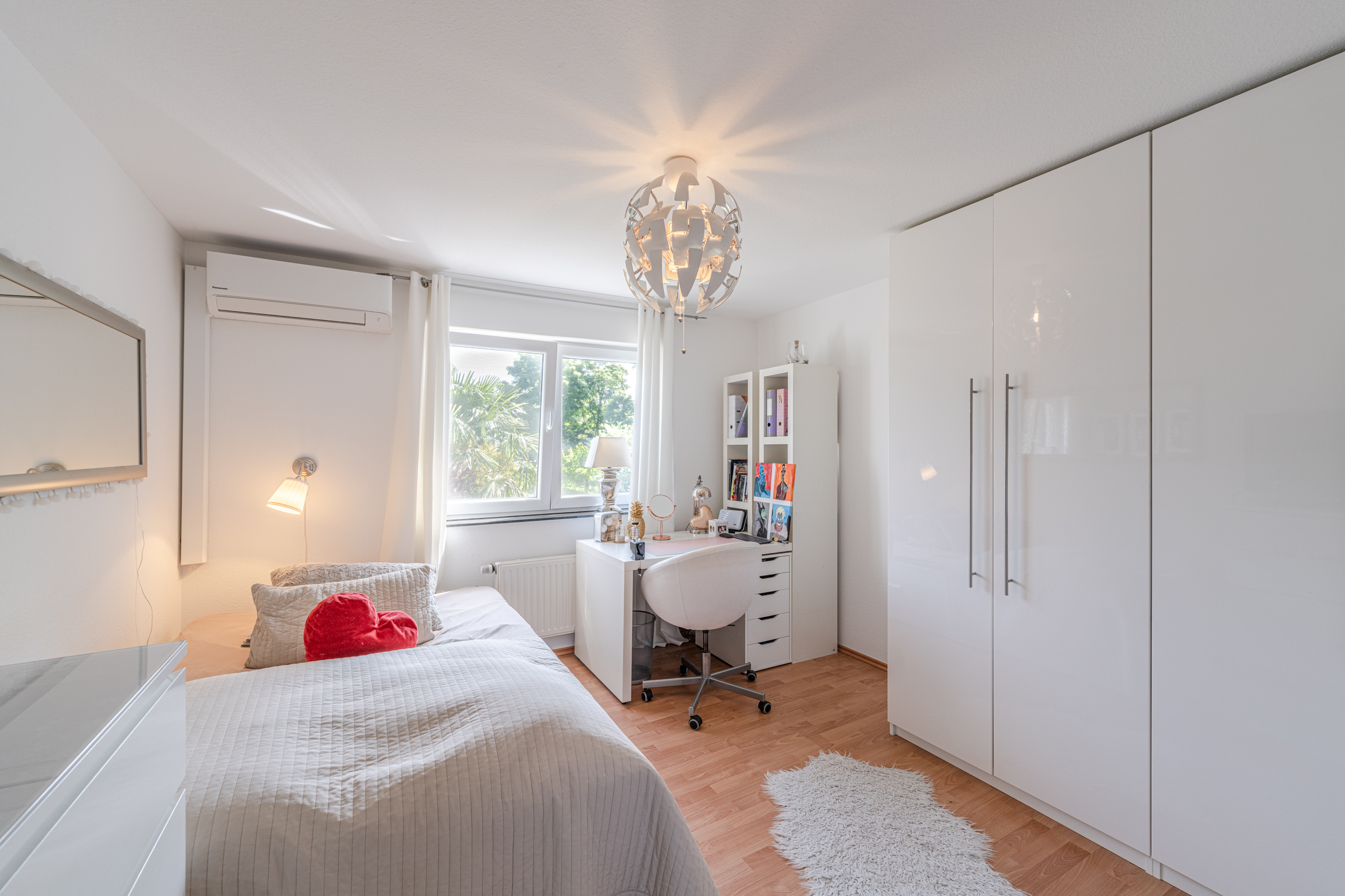 Helles Schlafzimmer mit Bett, Schreibtisch, großem Schrank und Fenster mit Blick ins Grüne.