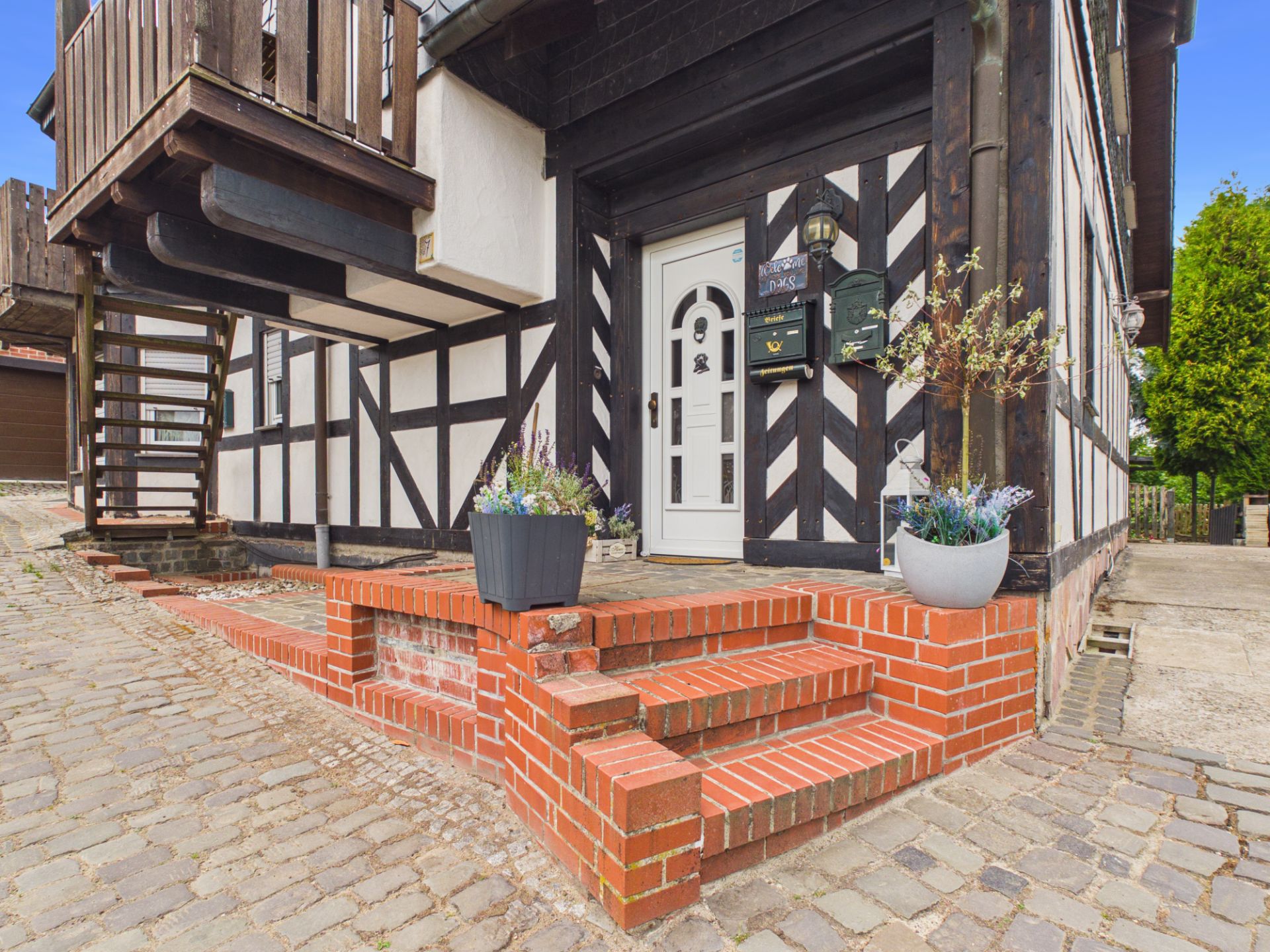 Eingang eines Fachwerkhauses mit roter Backsteintreppe und Blumenkübeln.