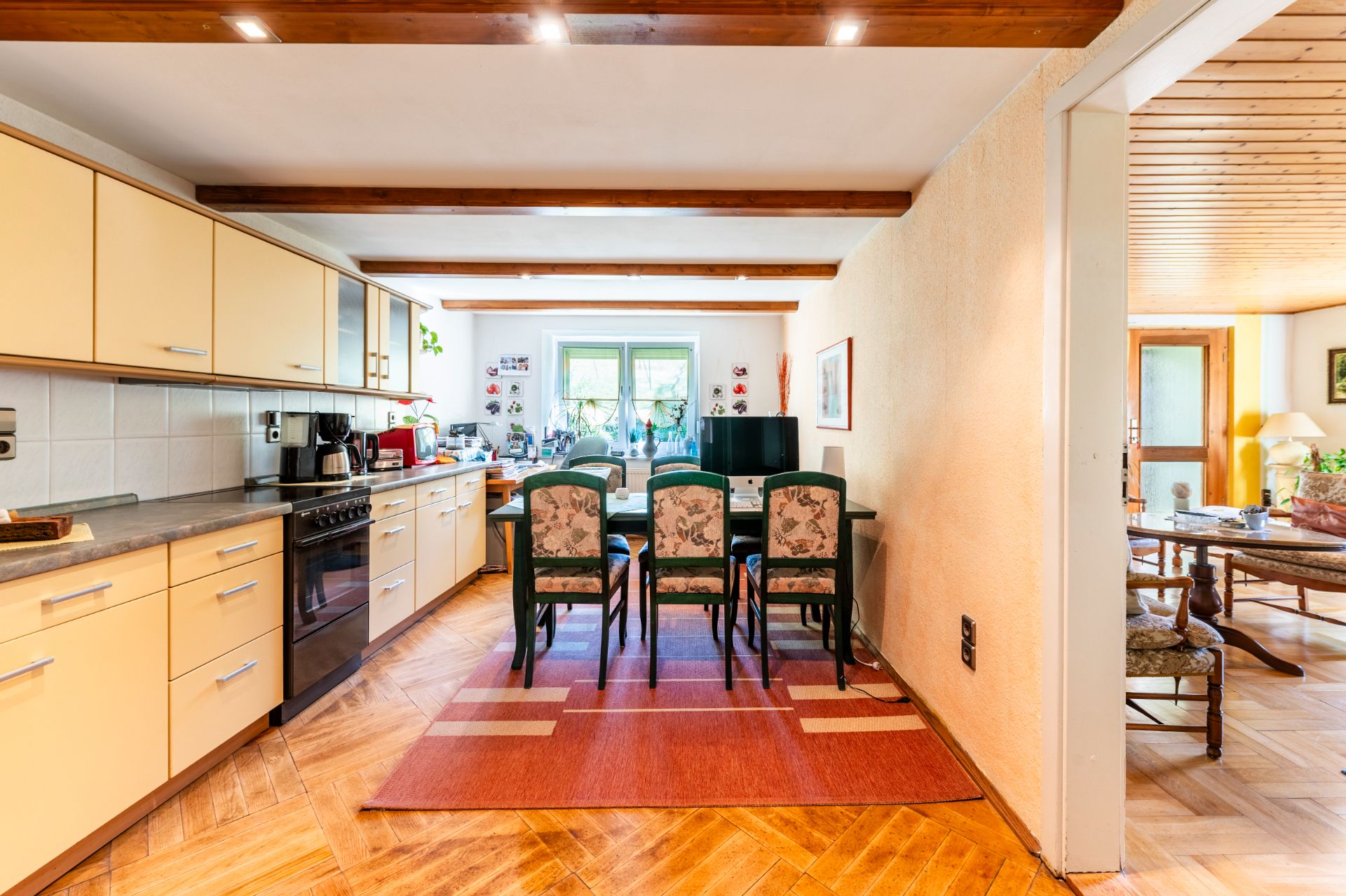 Küche mit Esstisch und vier Stühlen, Fenster im Hintergrund, angrenzendes Wohnzimmer.