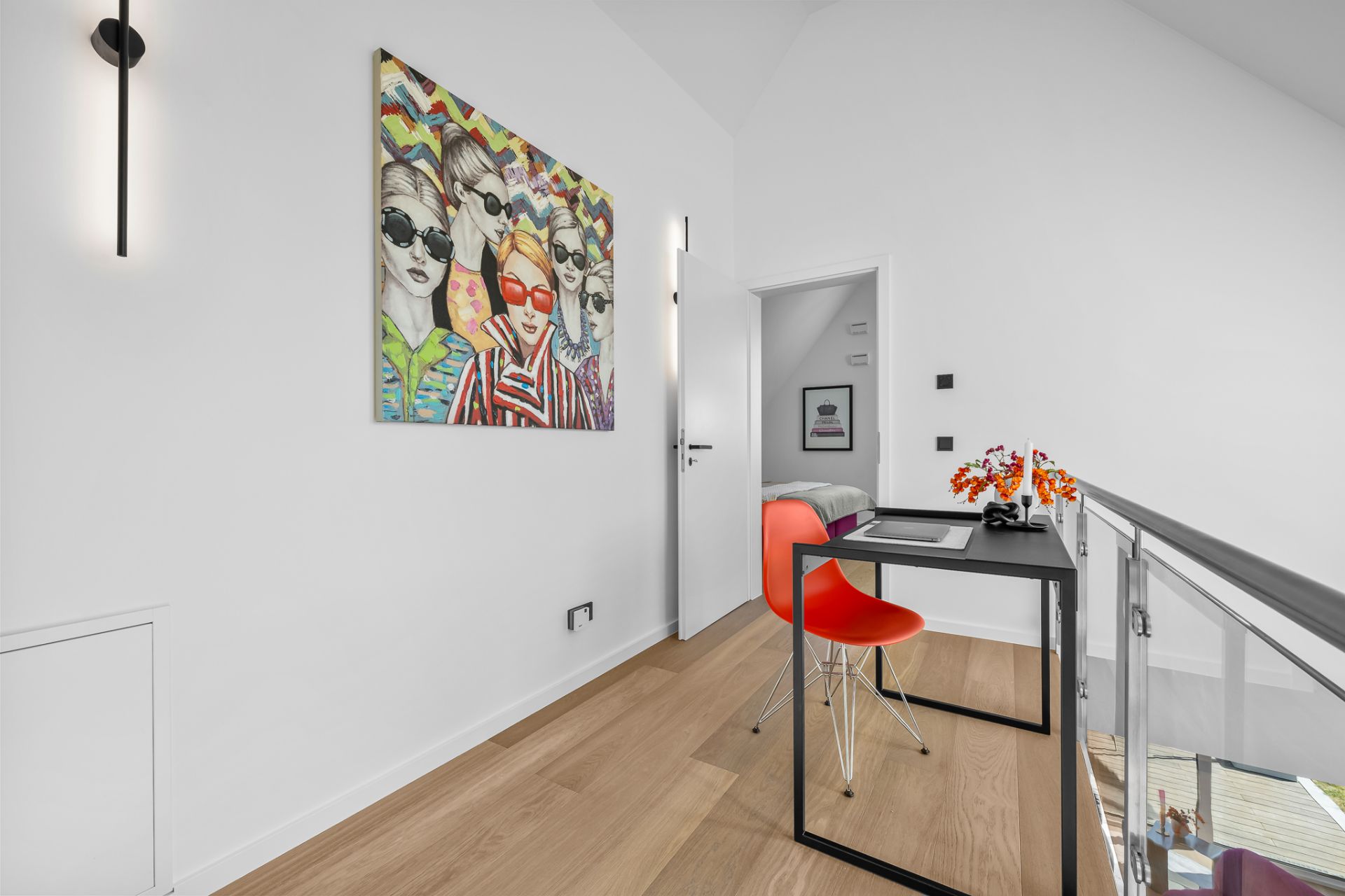 Heller Raum mit Schreibtisch, rotem Stuhl und farbigem Bild an der weißen Wand.