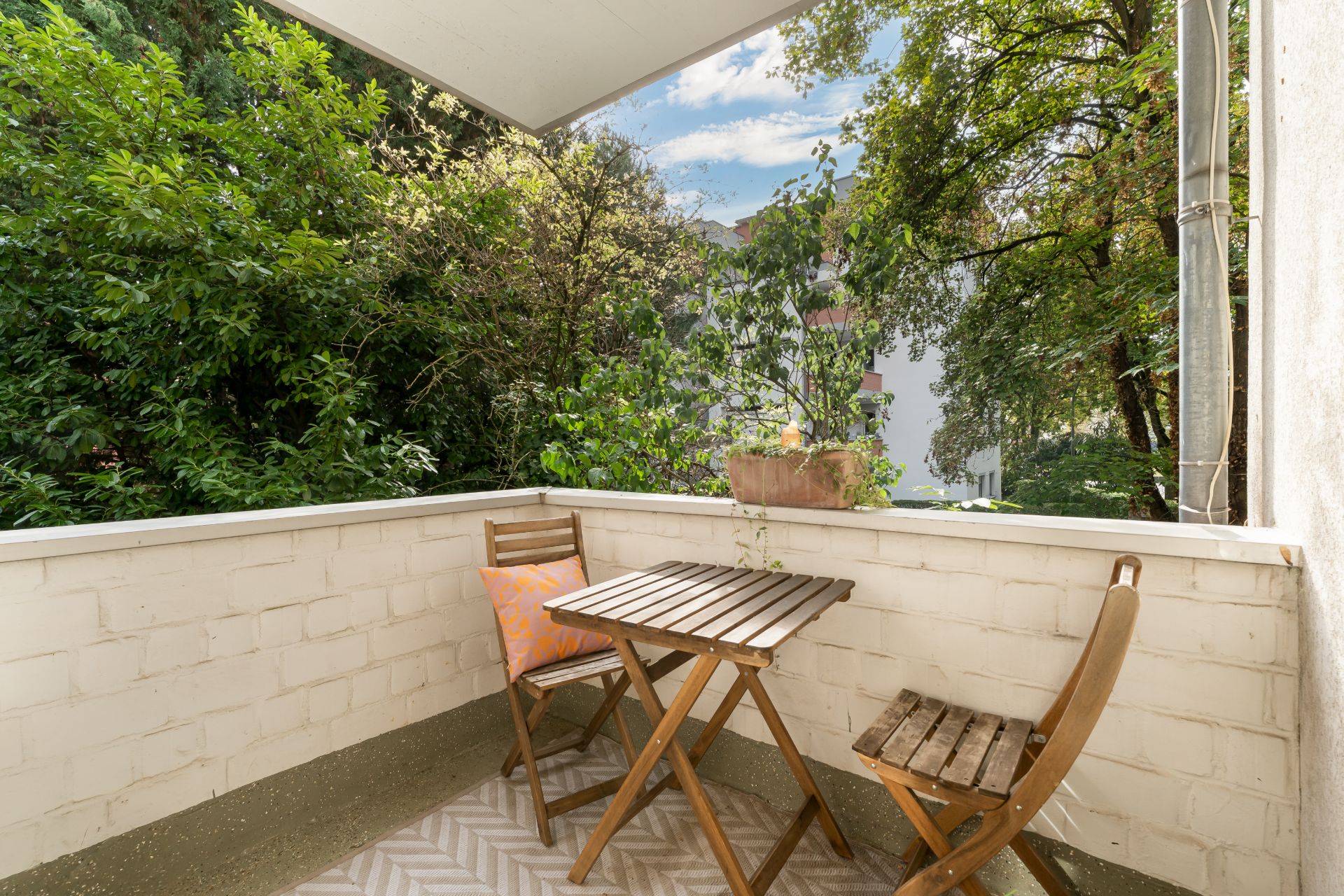 Kleiner Balkon mit zwei Holzstühlen, Tisch und Blick ins Grüne.