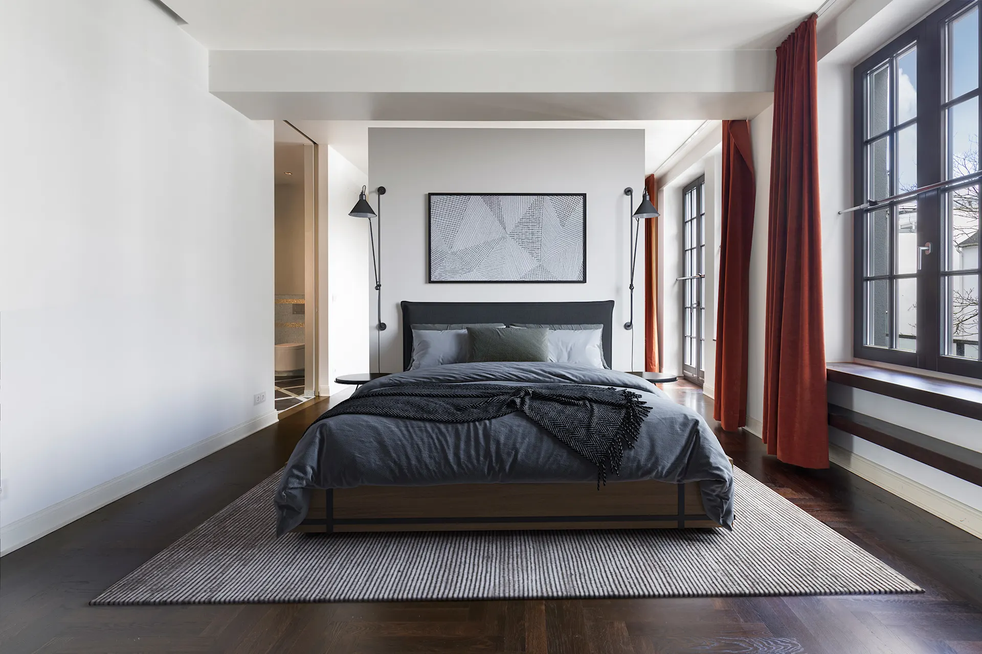 Modernes Schlafzimmer mit großem Bett, zwei Fenstern und roten Vorhängen.