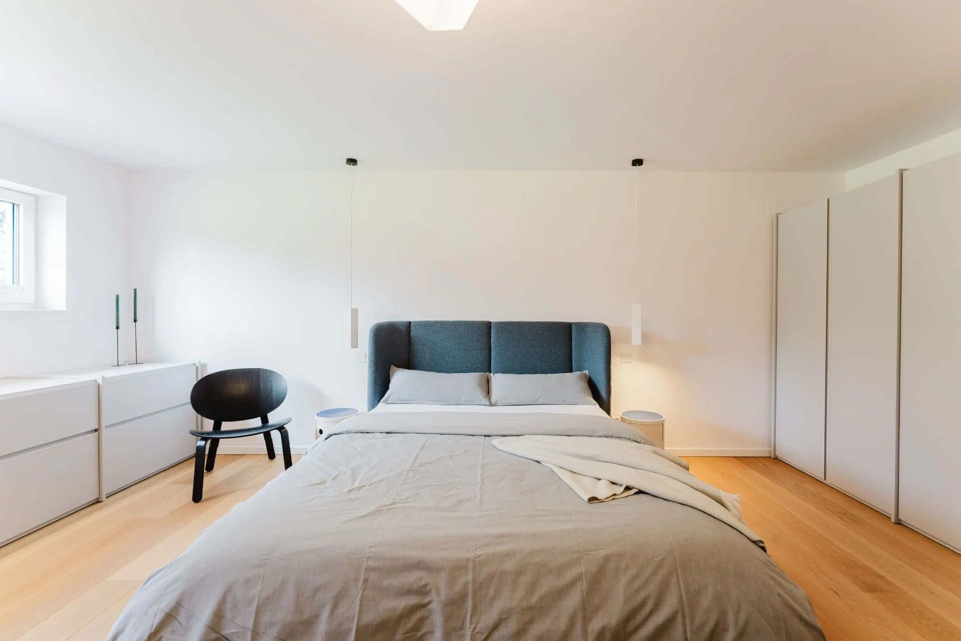 Modernes Schlafzimmer mit Doppelbett, Kleiderschrank, Kommode und Stuhl auf hellem Holzboden.