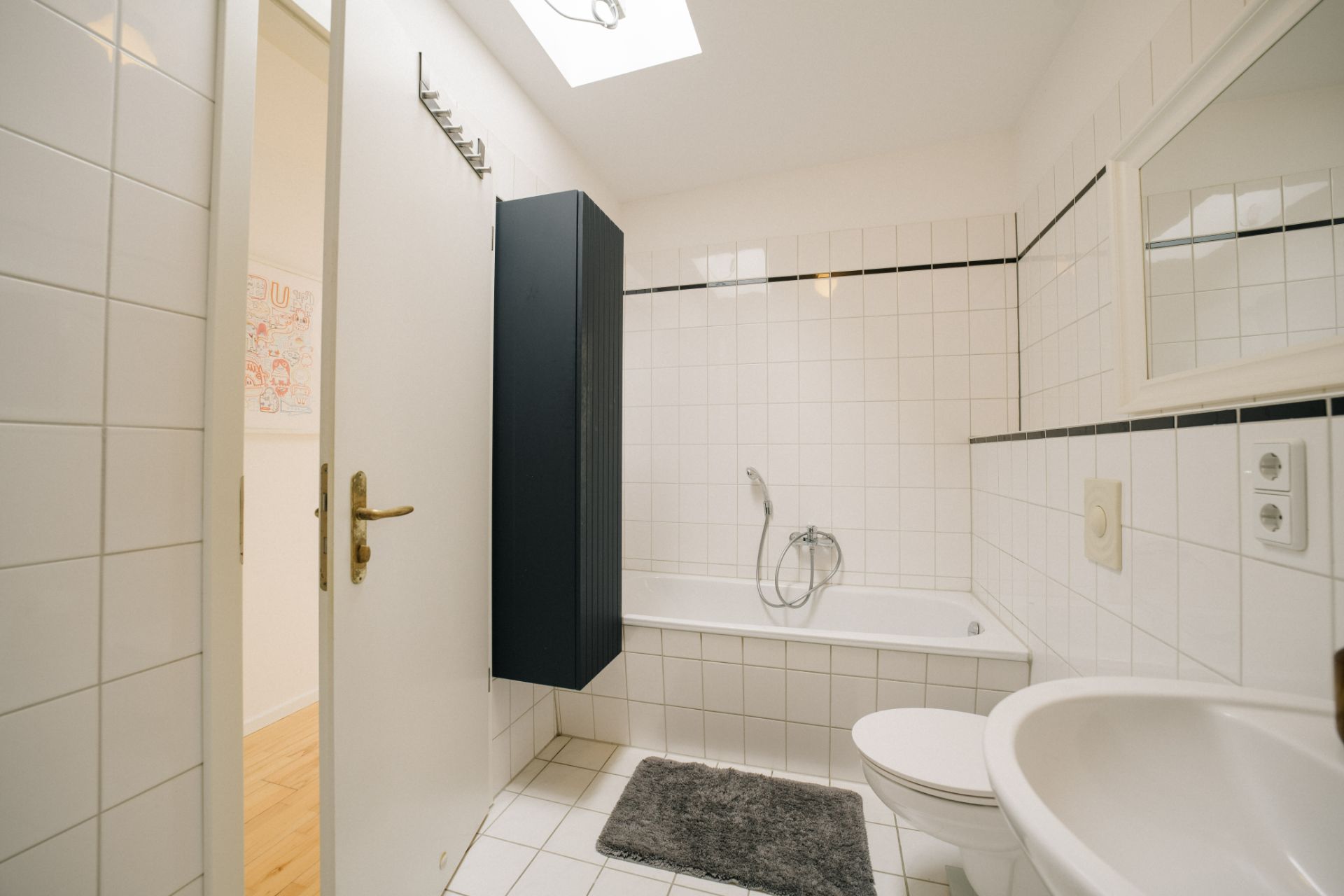 Helles Badezimmer mit Badewanne, Waschbecken, Toilette und Spiegel, weiße Fliesen an Wand und Boden.