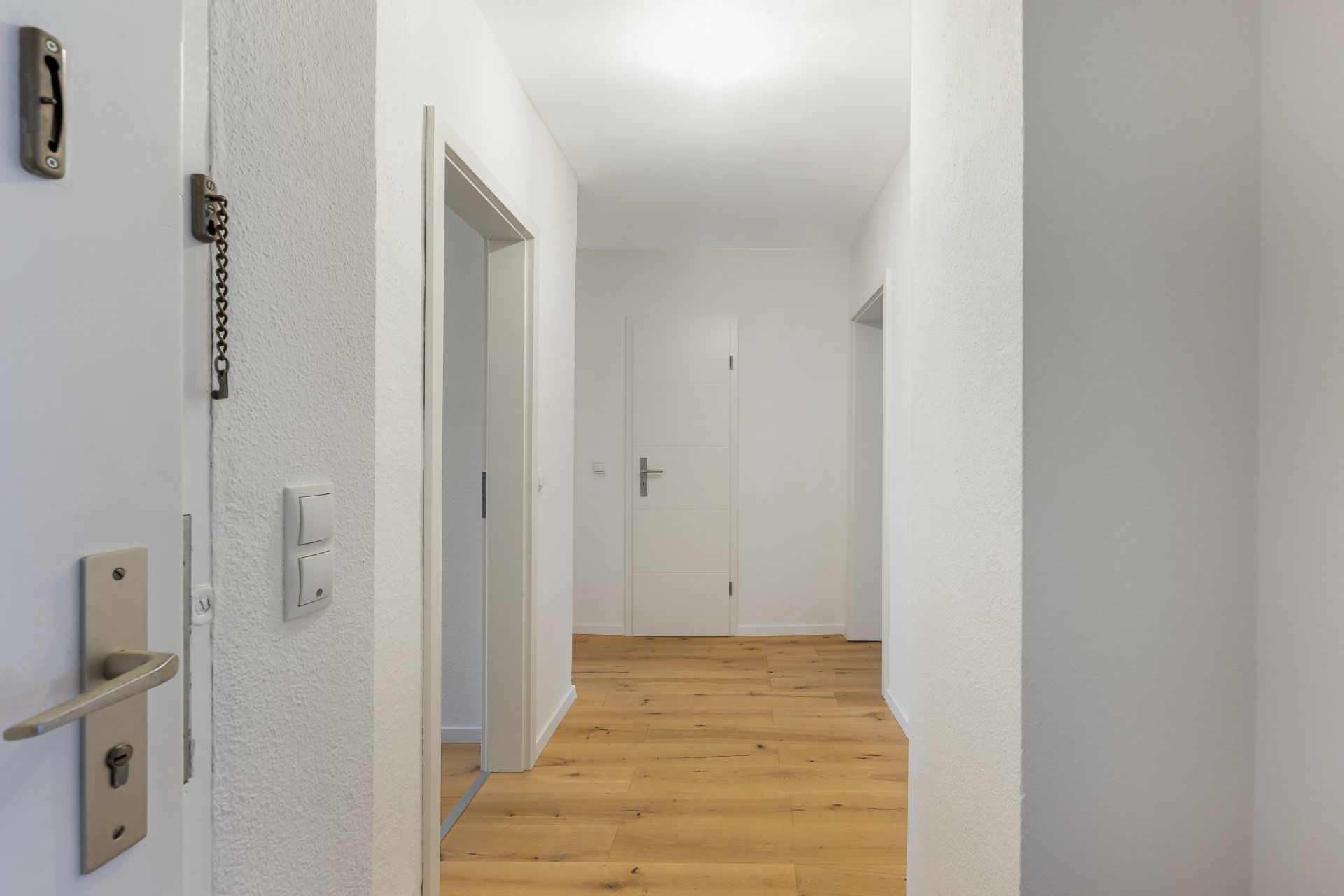 Heller Flur mit Holzboden und mehreren weißen Türen in einer Wohnung.