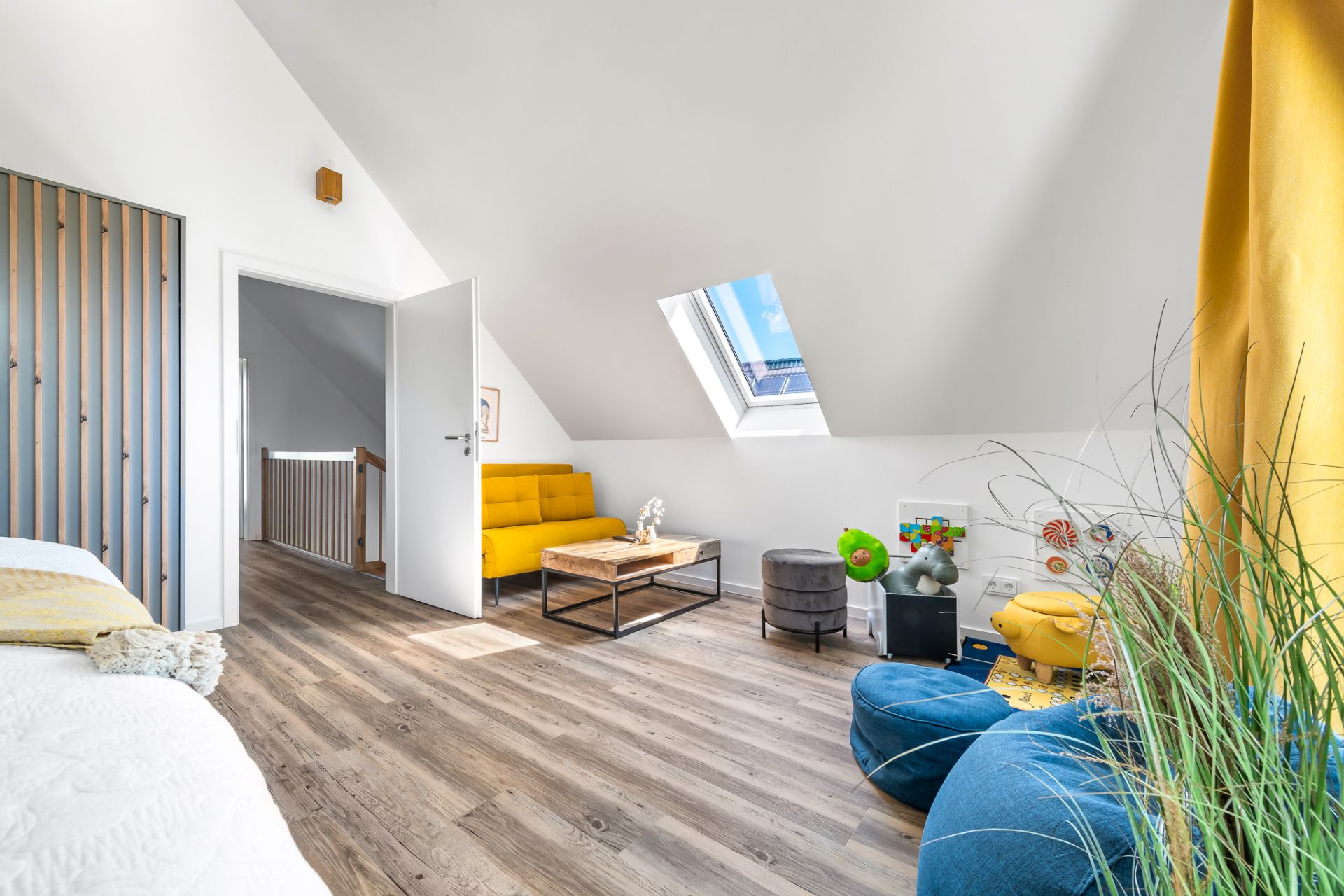Helles Dachzimmer mit gelbem Sofa, Couchtisch, Sitzsäcken und Dachfenster.