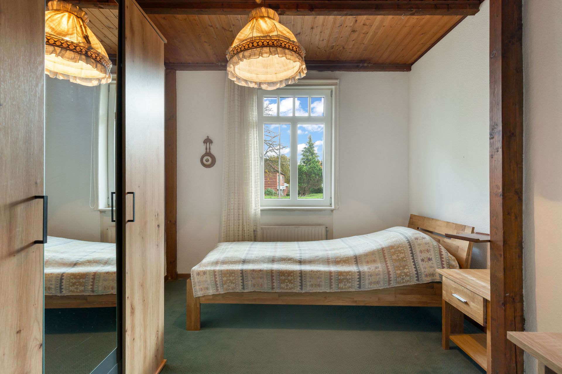 Schlafzimmer mit Einzelbett, Holzmöbeln, Fenster und Deckenlampe.