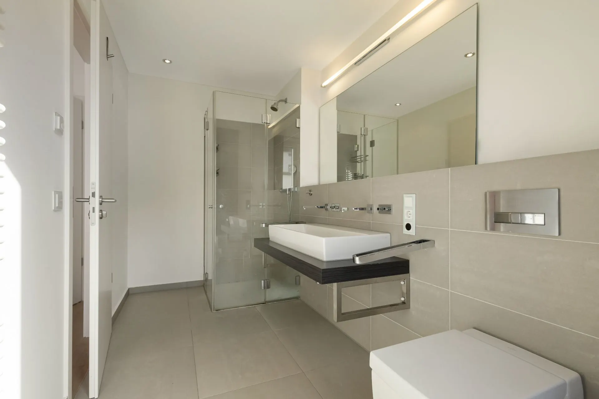 Modernes Badezimmer mit großem Spiegel, rechteckigem Waschbecken und Glasdusche.