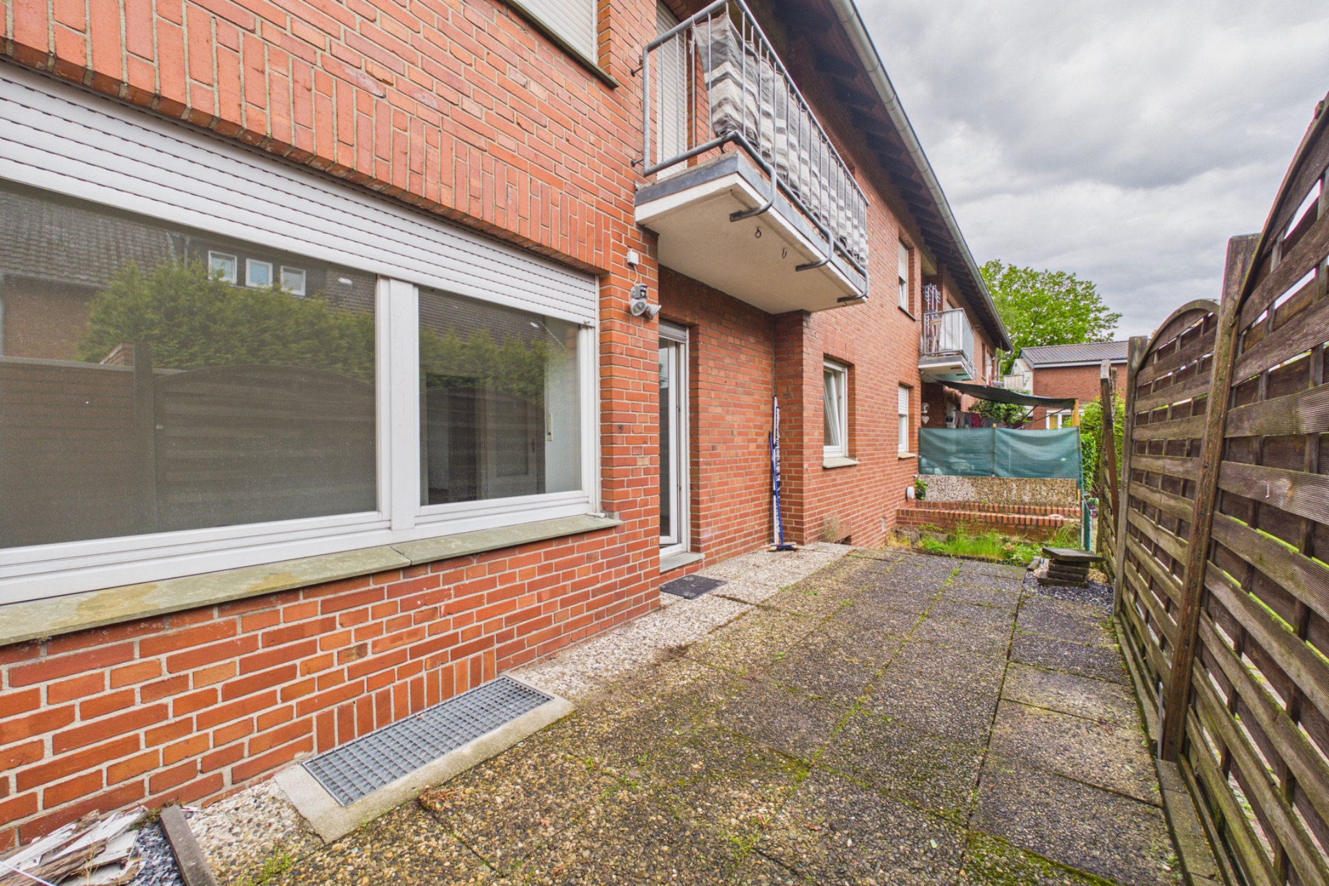 Gepflasterte Terrasse neben einer roten Backsteinfassade mit Fenstern und Balkon.
