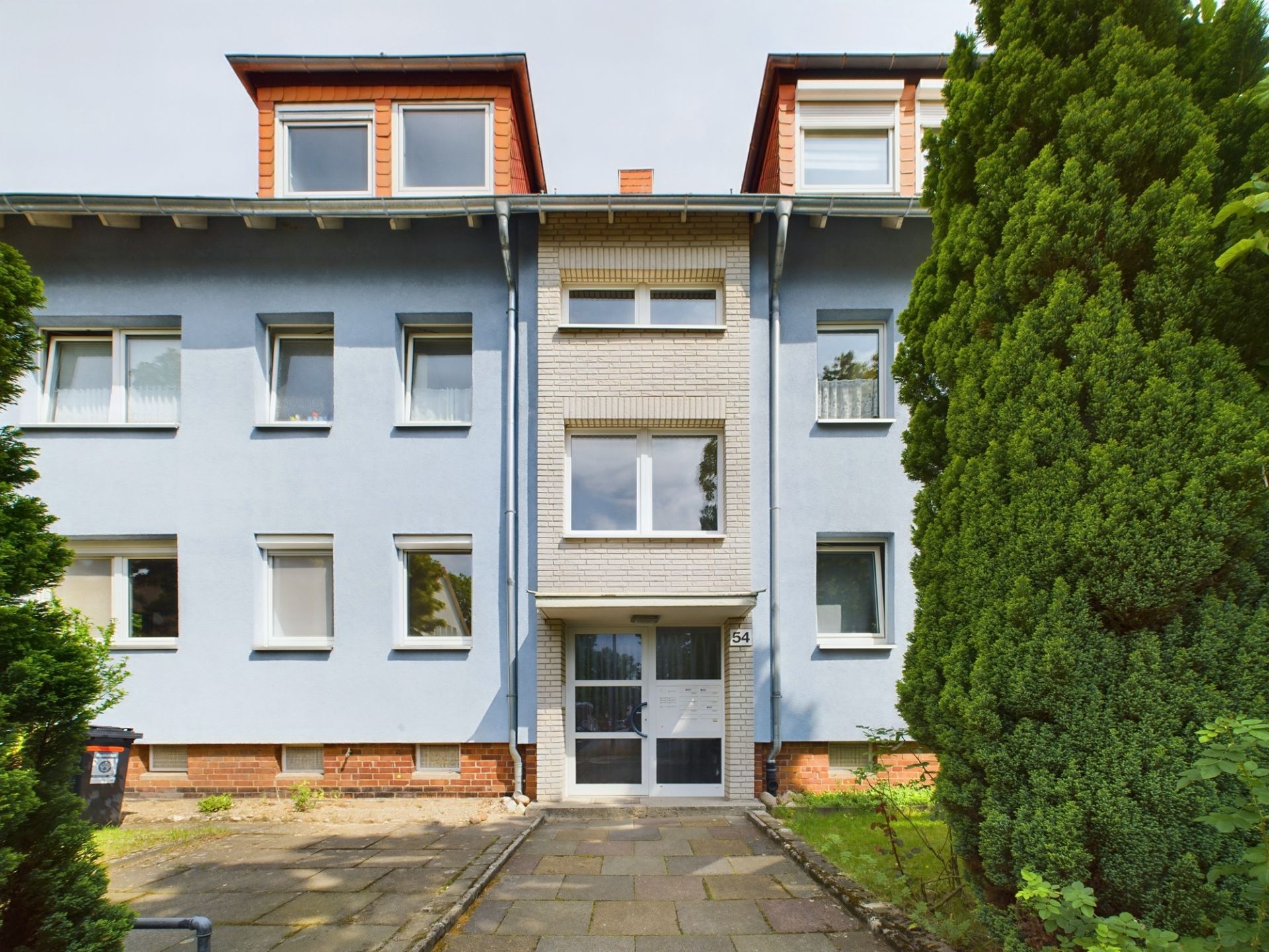 Vorderansicht eines mehrstöckigen Wohnhauses mit blauem Putz und großen Fenstern.