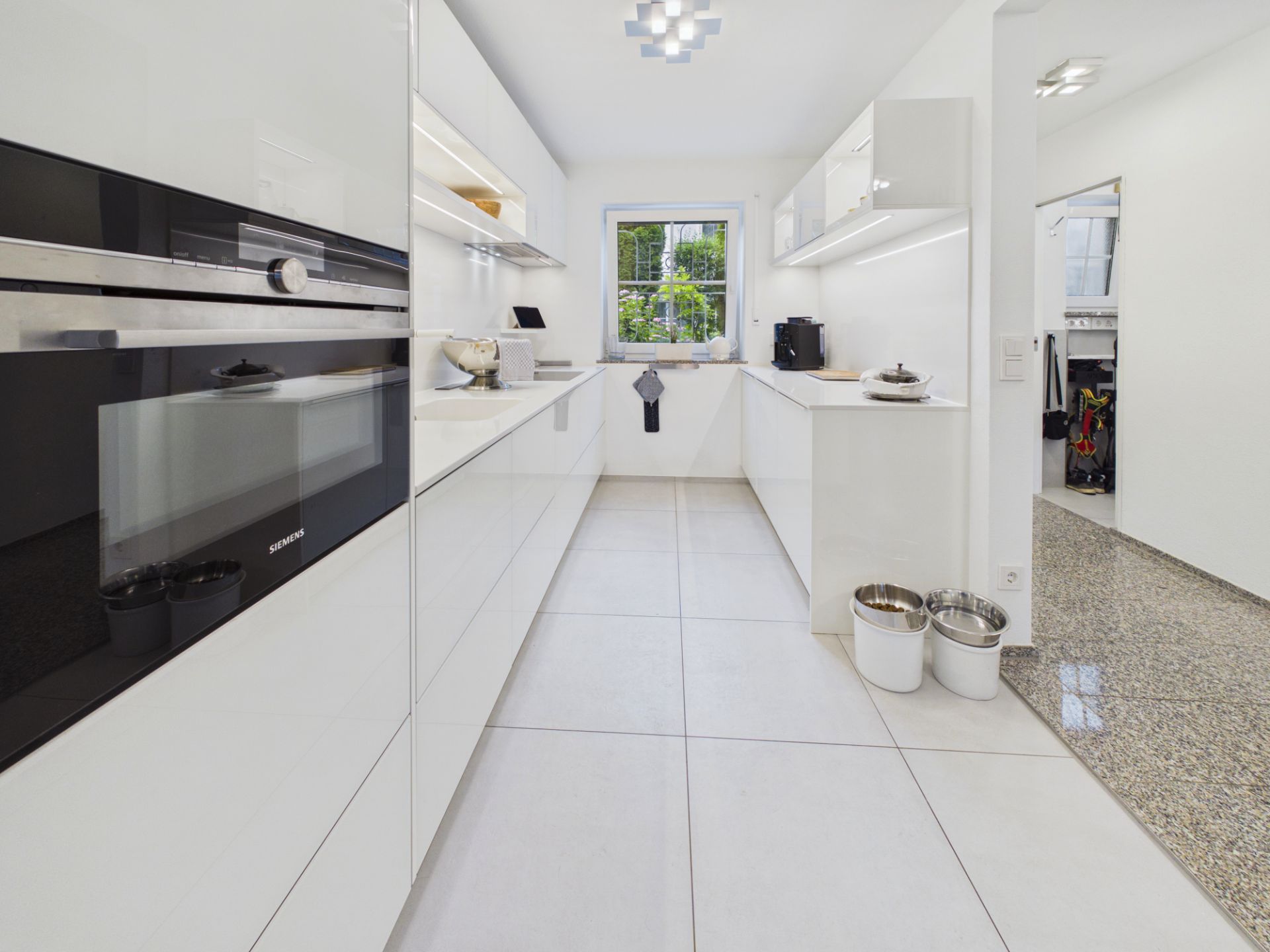 Moderne, weiße Küche mit großem Fenster und eingebauten Geräten.