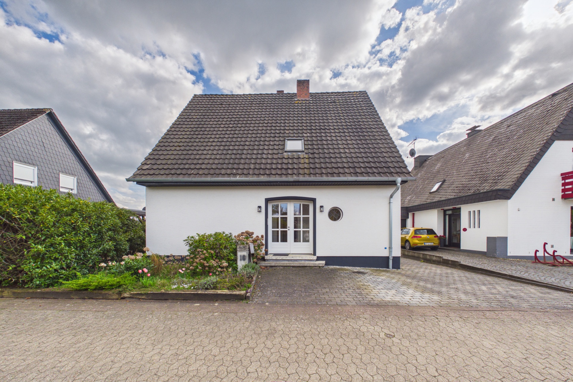 Vorderansicht eines Einfamilienhauses mit Garten, Einfahrt und grauem Dach.
