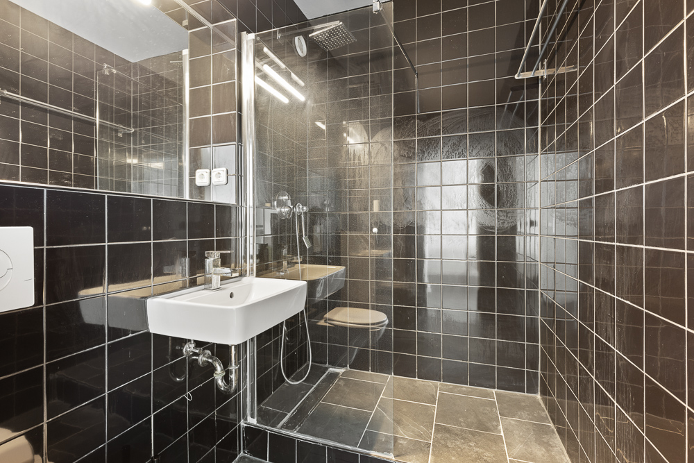 Modernes Badezimmer mit schwarzen Fliesen, Waschbecken, Toilette und offener Dusche.