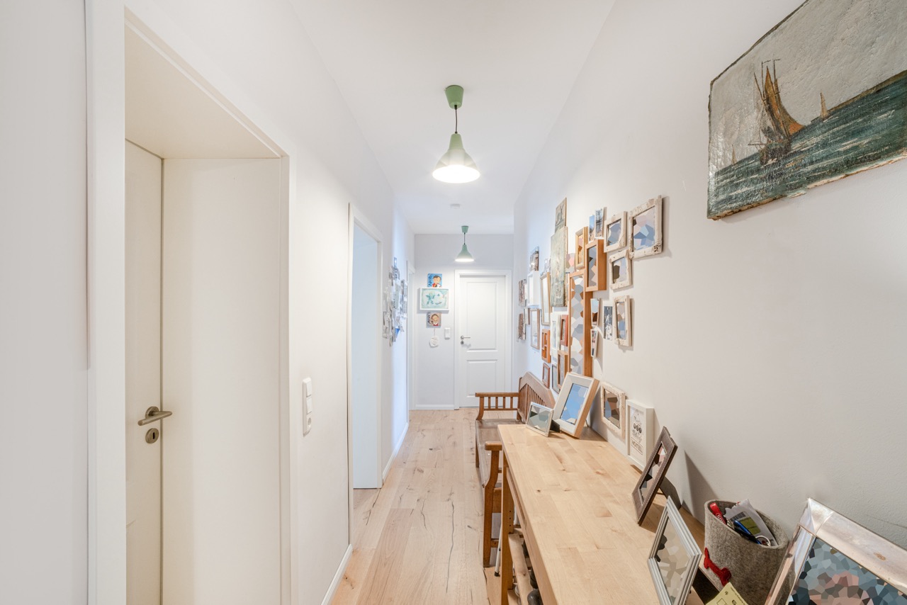 Heller Flur mit Holzboden, Bildern an der Wand und einem Tisch mit Bildern und Dekoration.