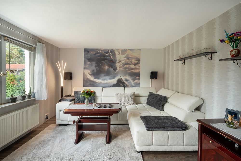 Helles Wohnzimmer mit weißem Ecksofa, Couchtisch, Blumen und großem Wandgemälde.