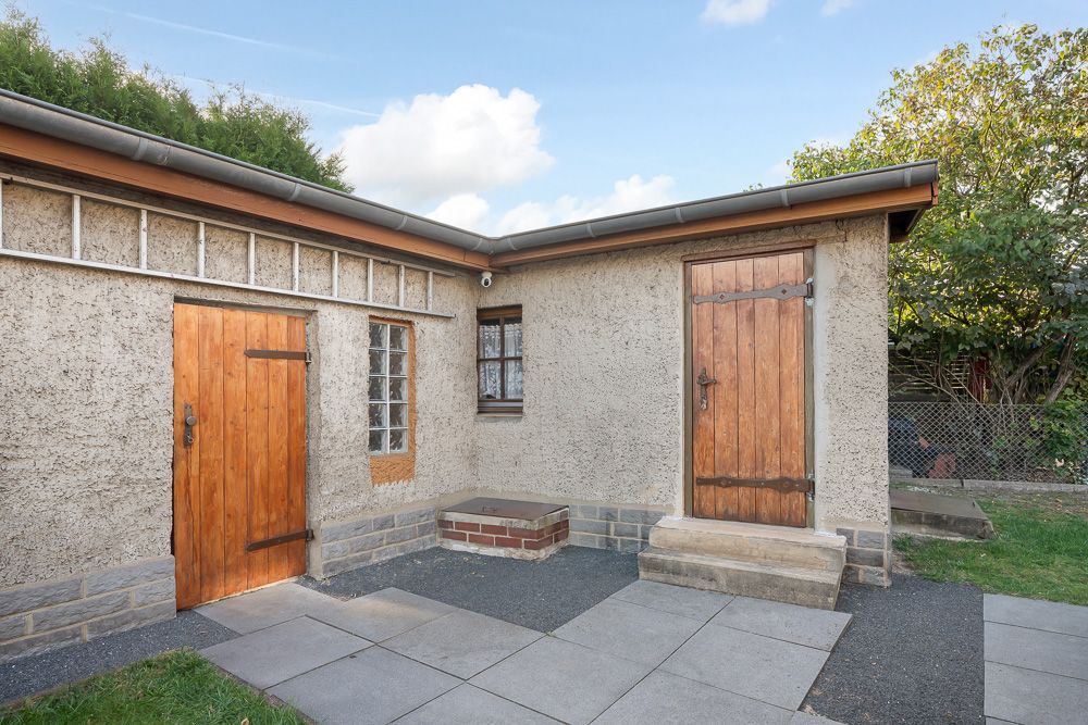 Einfache Hausaußenwand mit zwei Holztüren, kleinem Fenster und gepflastertem Vorplatz.