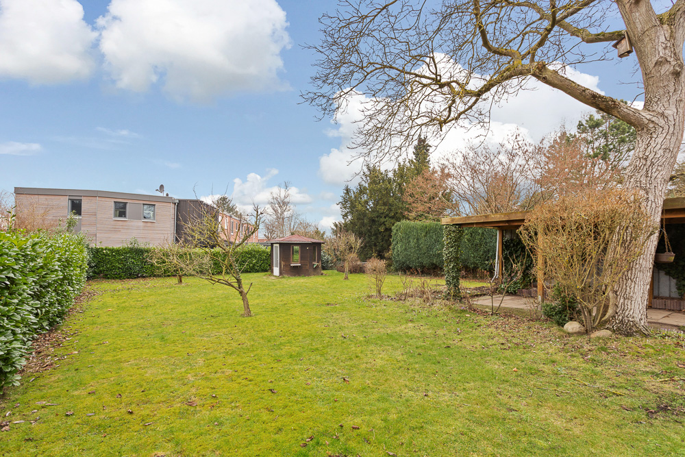 Großer Garten mit Rasen, Bäumen, Gartenhaus und überdachter Terrasse an einem Wohnhaus.