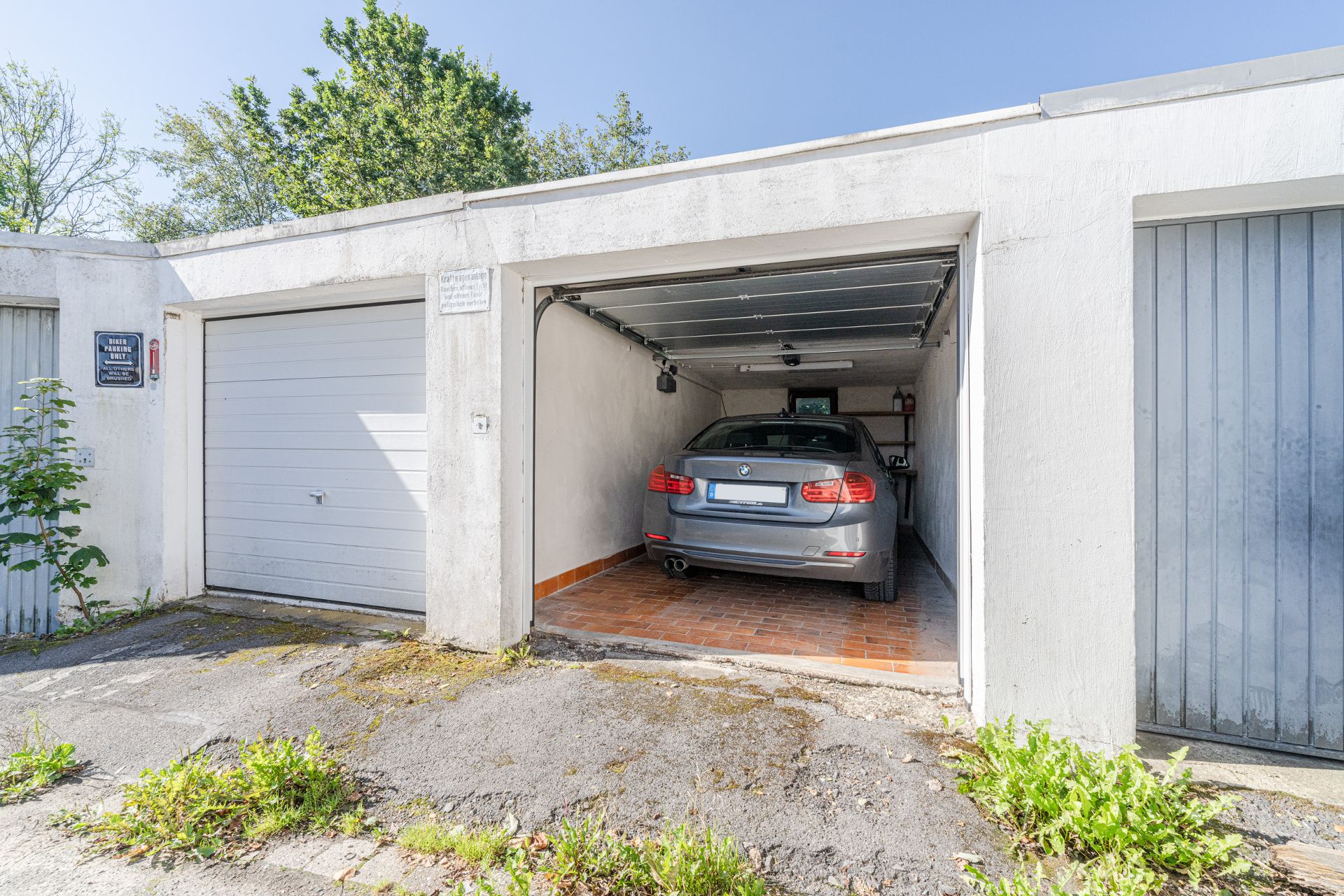 Graues Auto steht in einer offenen Garage mit weißer Fassade und Fliesenboden.