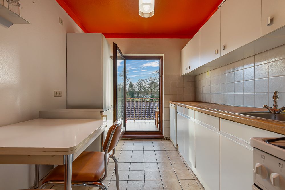 Helle Küche mit weißen Schränken, Tisch, zwei Stühlen und Zugang zu einem Balkon mit Ausblick.