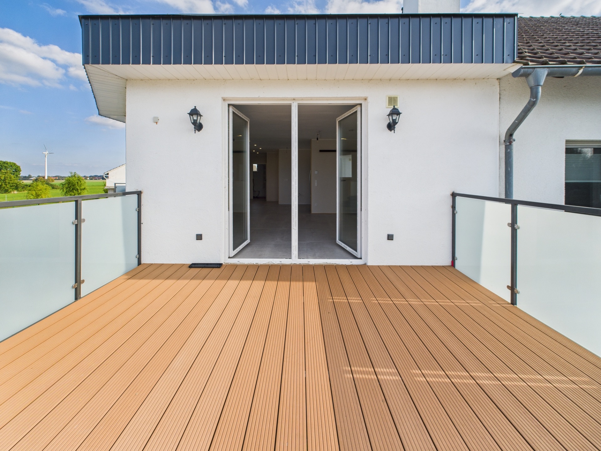 Große Terrasse mit Holzboden, Glasgeländer und Zugang durch doppelte Glastür.