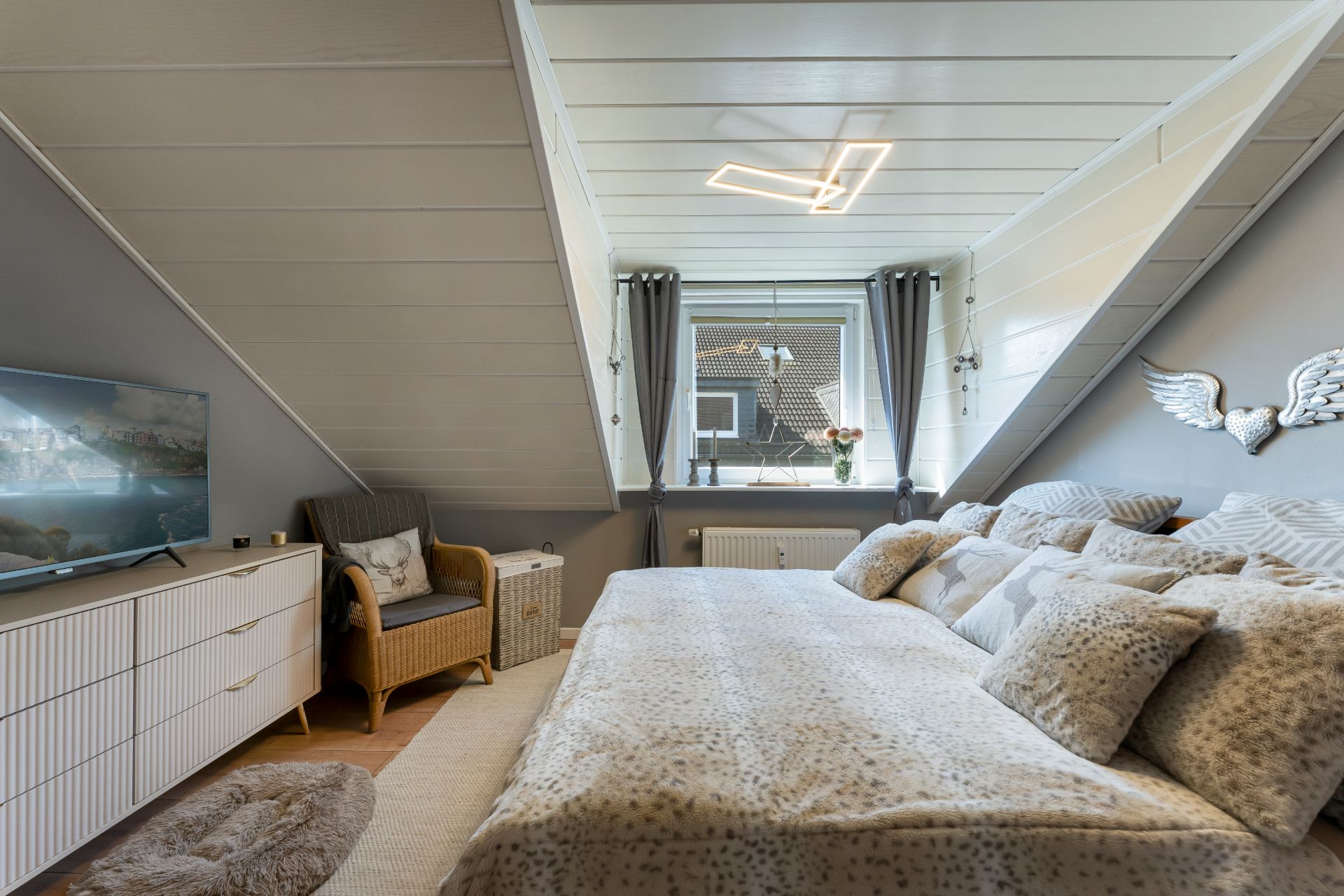 Gemütliches Schlafzimmer mit Doppelbett, TV, Sessel und Fenster mit Vorhängen.