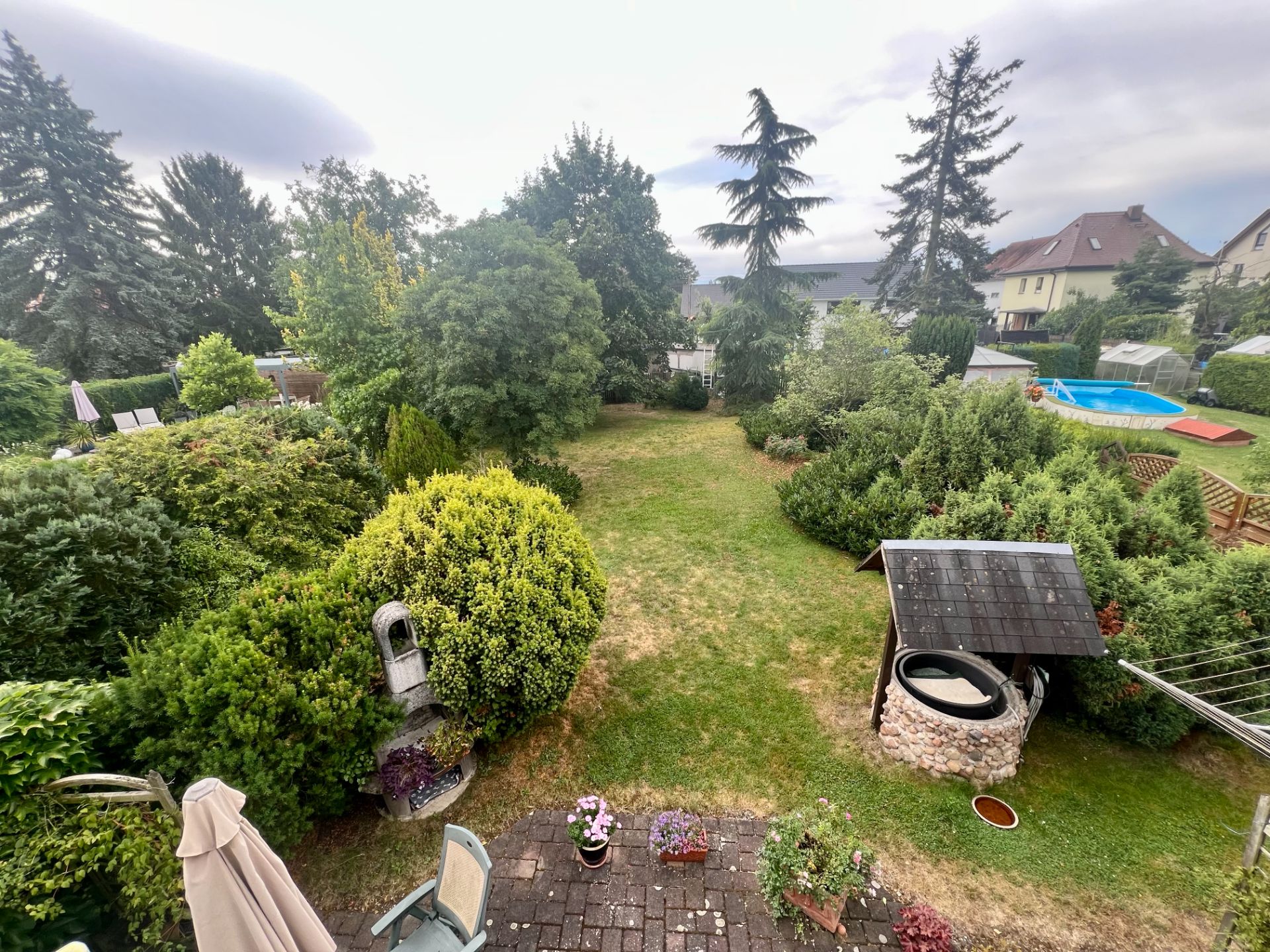 Großer Garten mit Brunnen, vielen Büschen und Bäumen, Blick von einer Terrasse.