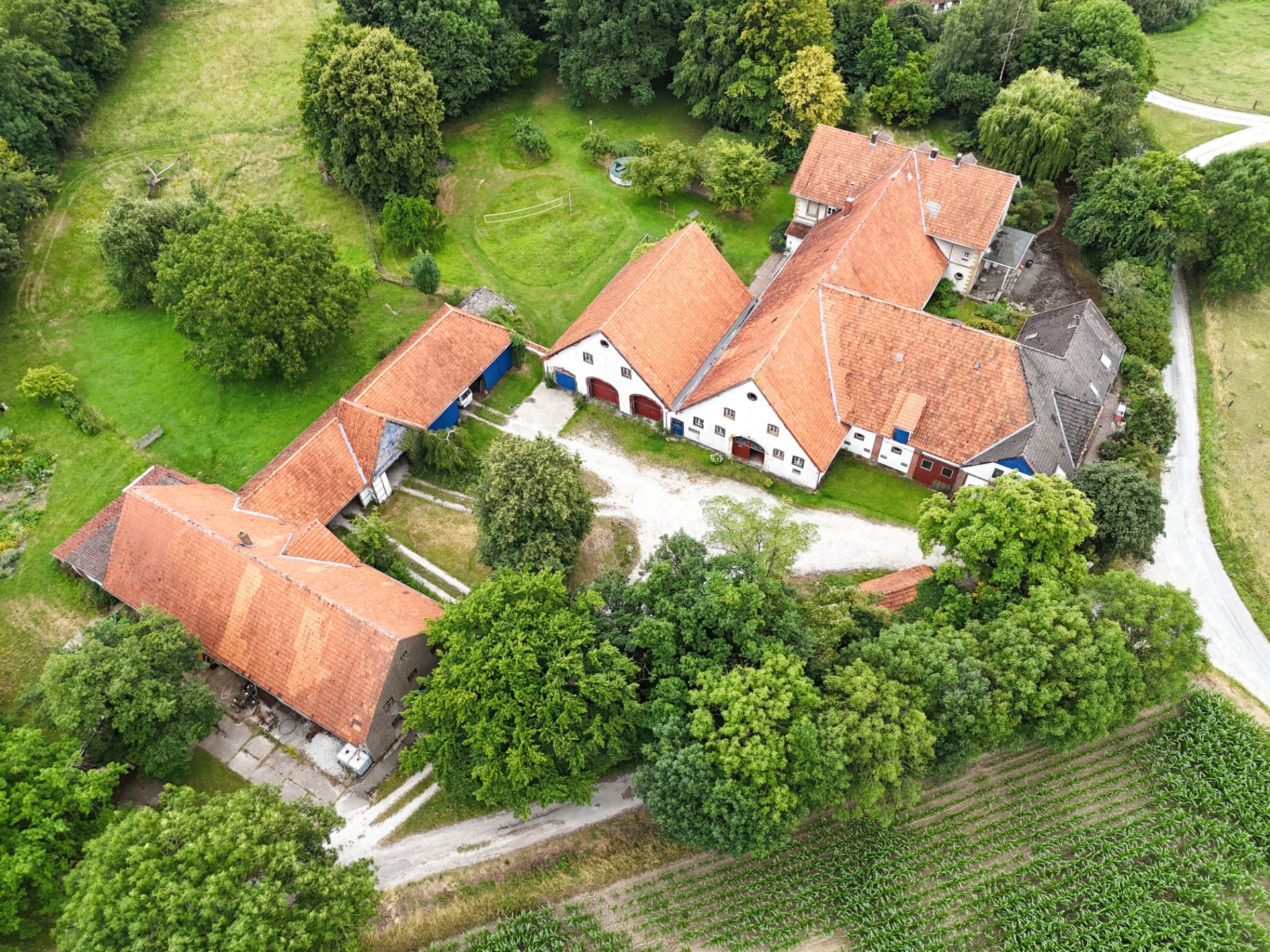 Luftaufnahme eines Bauernhofs mit roten Dächern, umgeben von Bäumen und Wiesen.