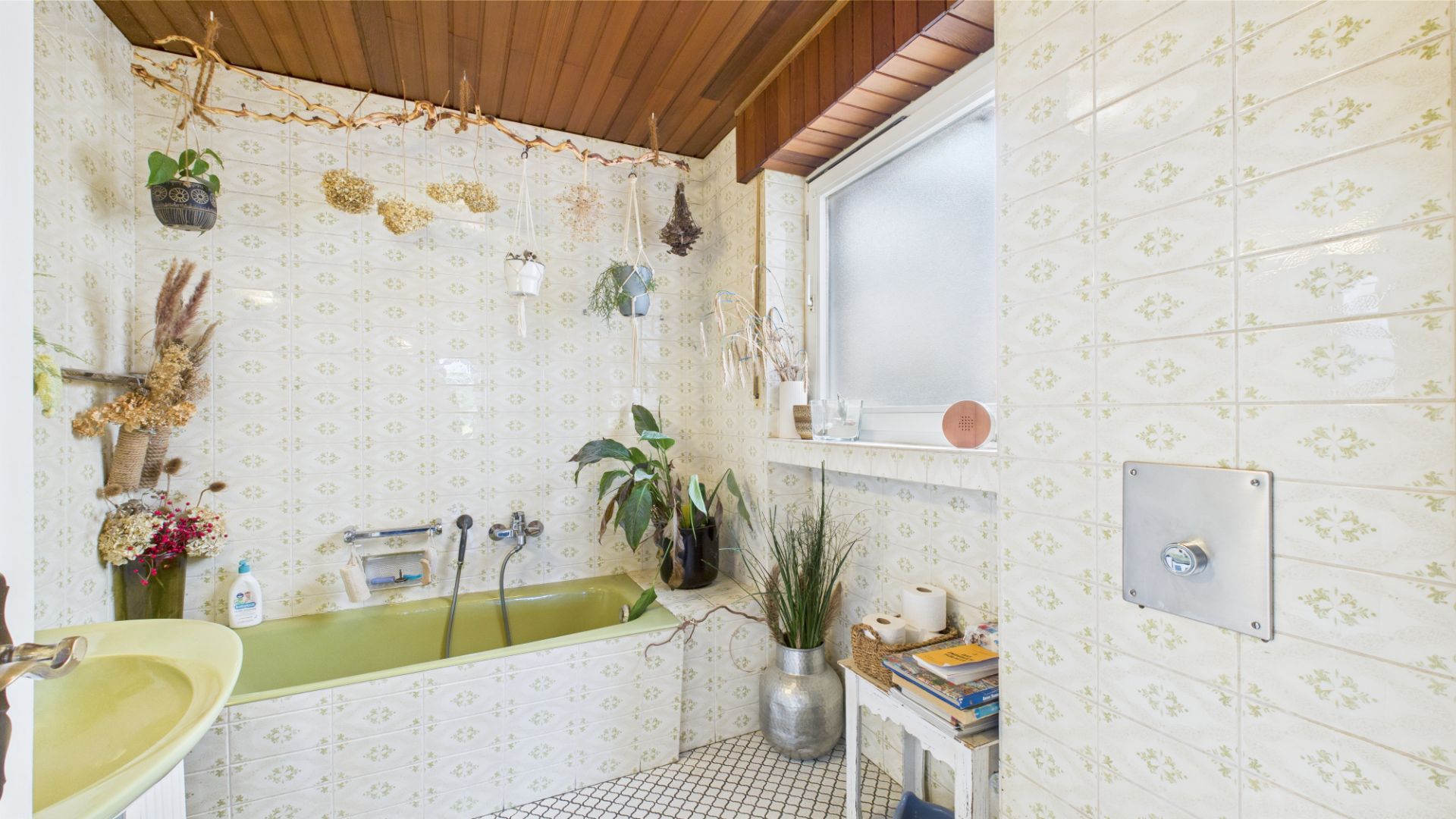 Badezimmer mit grüner Badewanne, vielen Pflanzen und gemusterten Fliesen.
