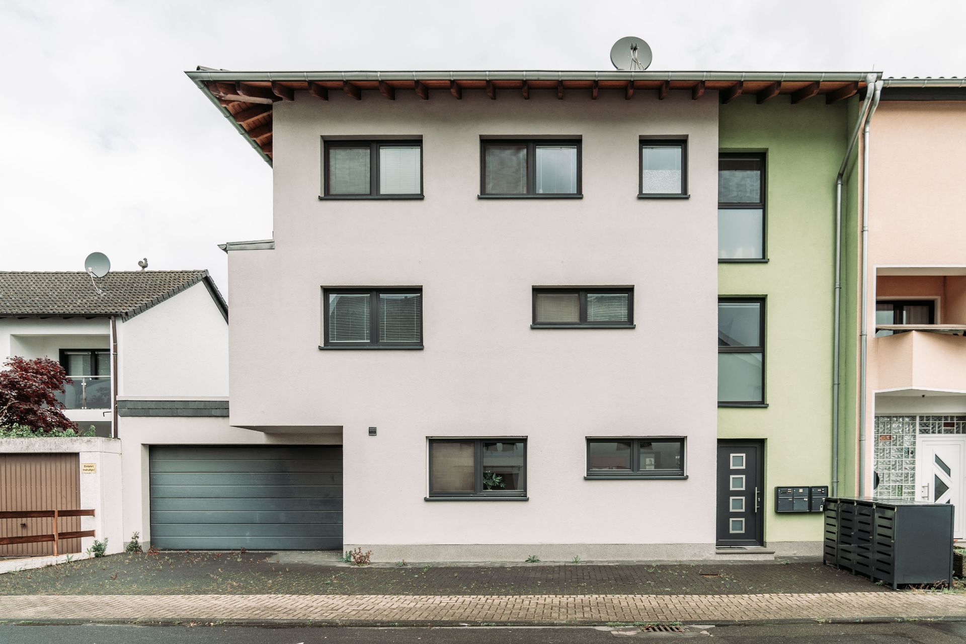 Modernes, dreistöckiges Wohnhaus mit flacher Fassade, vielen Fenstern und Garage.