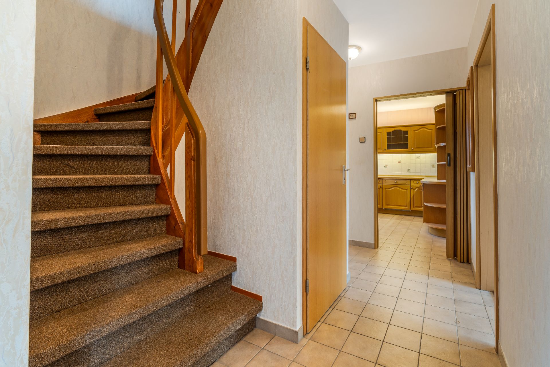 Flur mit Teppichtreppe und Blick in eine Küche mit Holzmöbeln.