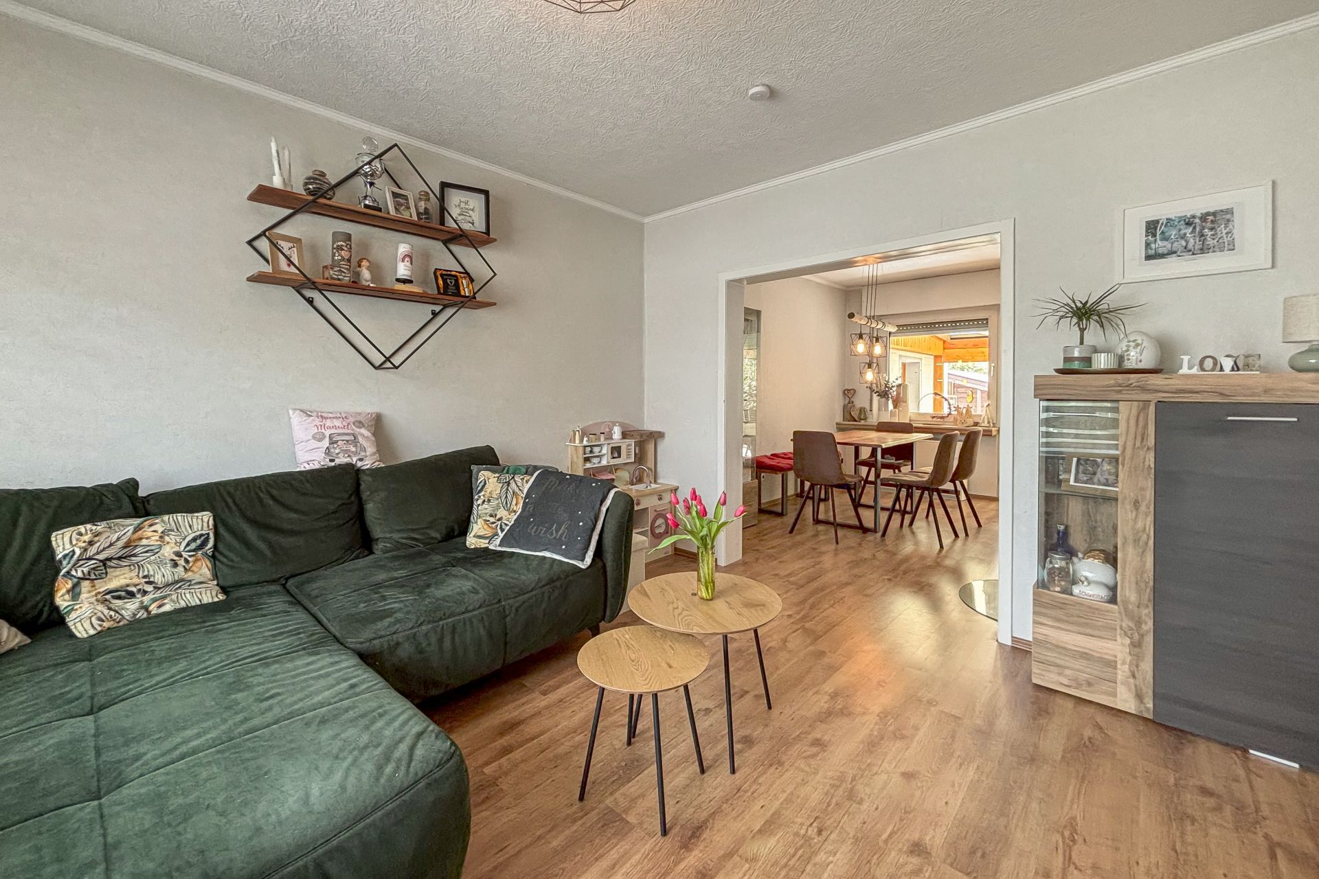 Gemütliches Wohnzimmer mit grünem Sofa, Holzboden und Blick ins Esszimmer.