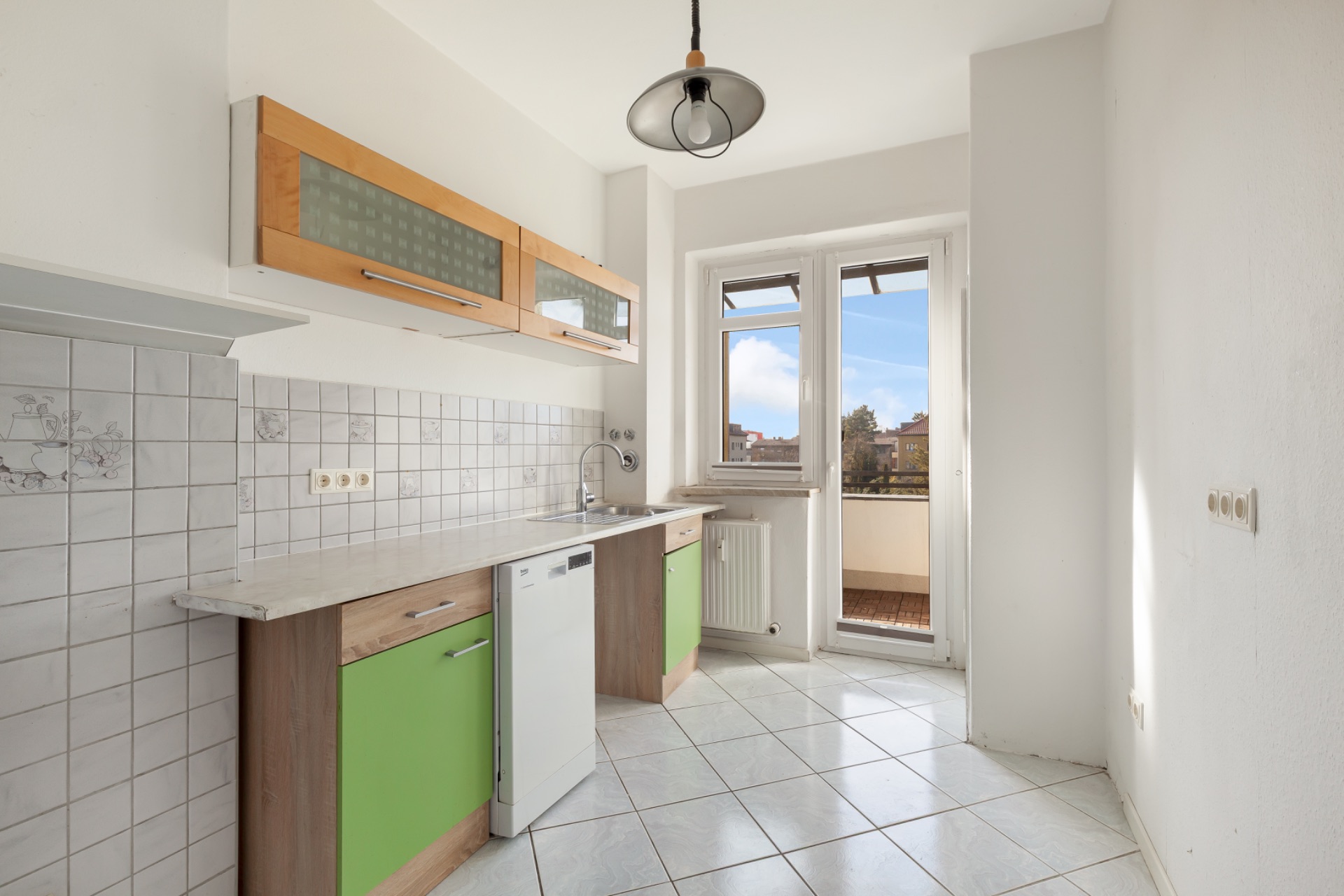 Helle Küche mit grünen Unterschränken, Wandfliesen, Spüle, Geschirrspüler und Zugang zu einem Balkon.