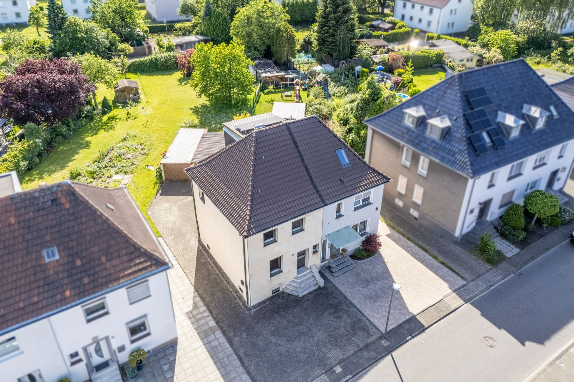 Luftaufnahme eines Einfamilienhauses mit Garten, Garage und Nachbarhäusern an einer ruhigen Straße.