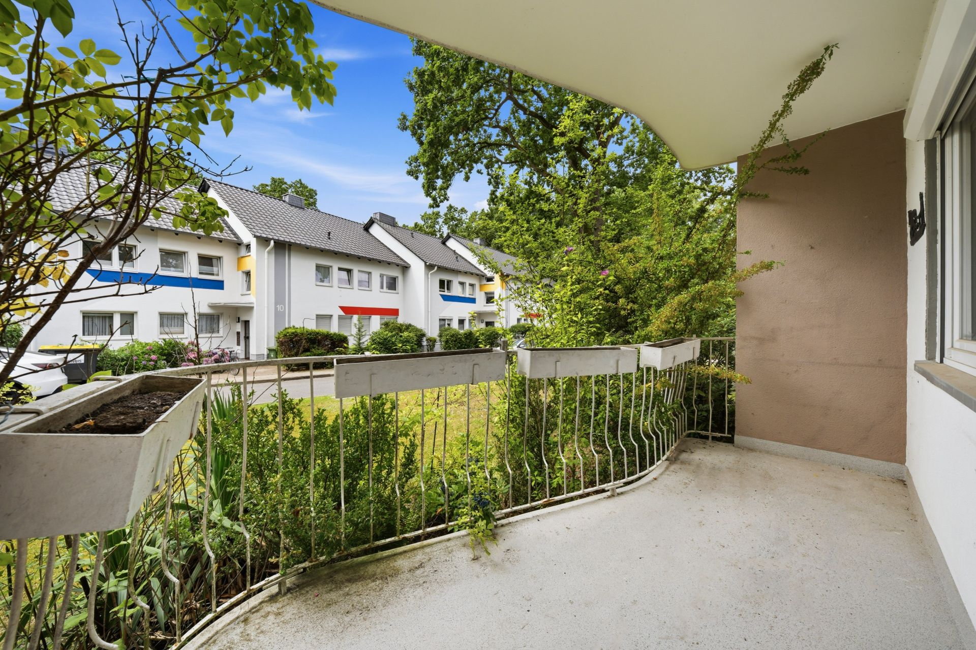 Balkon mit Blumenkästen und Blick auf grüne Hecke und Nachbarhäuser.