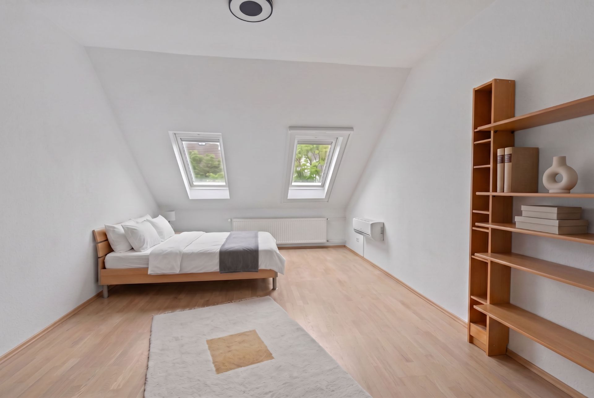 Helles Schlafzimmer mit Holzregal, Bett und zwei Dachfenstern.
