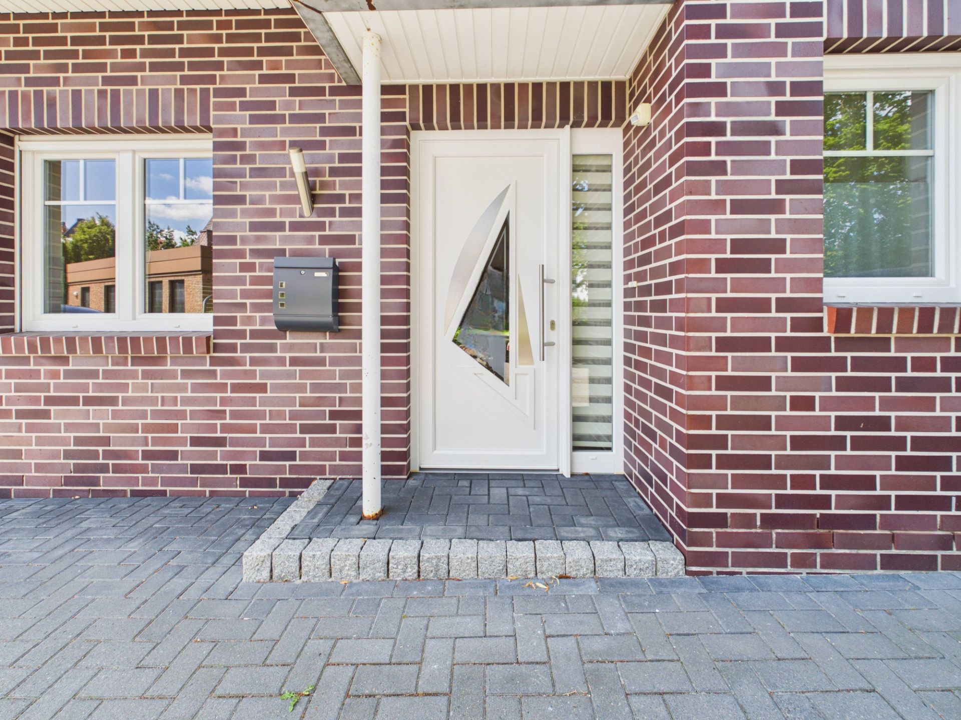 Eingang eines Hauses mit weißer Haustür, Klinkerwand und zwei Fenstern.