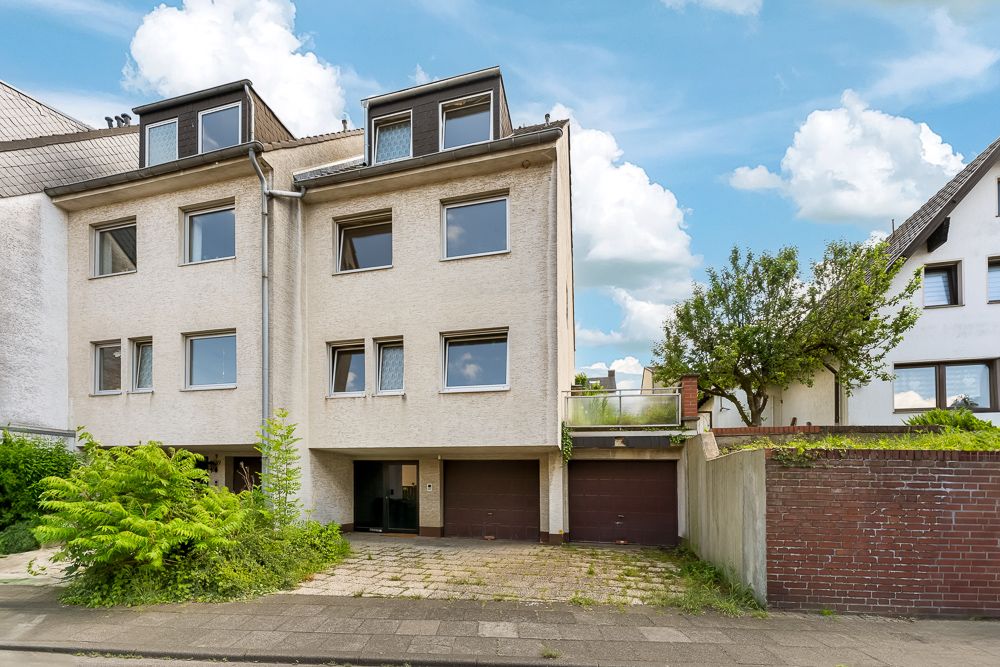 Vorderansicht eines dreistöckigen Wohnhauses mit Garagen und einigen Pflanzen im Vorgarten.