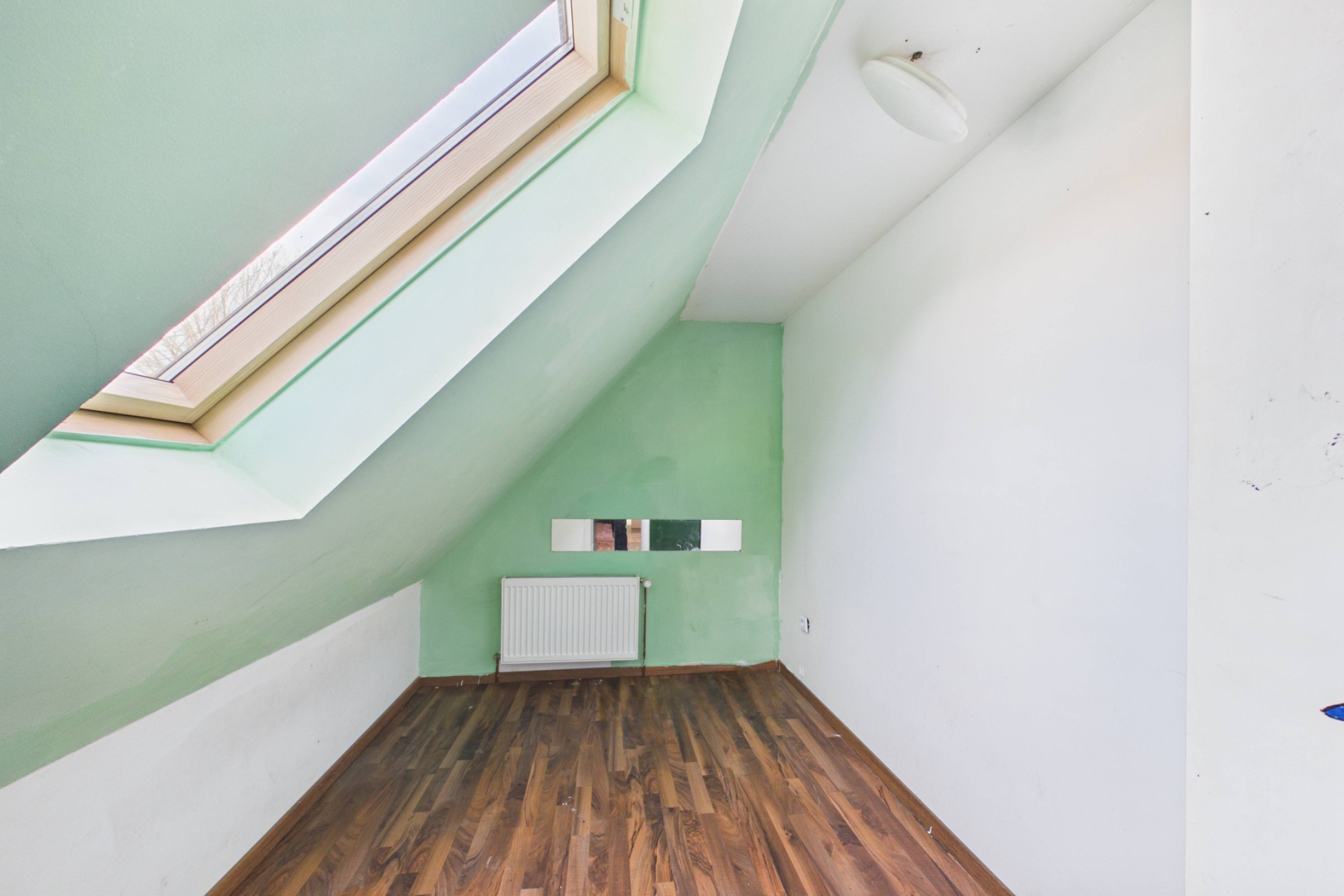 Kleines Zimmer mit Dachschräge, Dachfenster, grün-weißen Wänden und Holzfußboden.