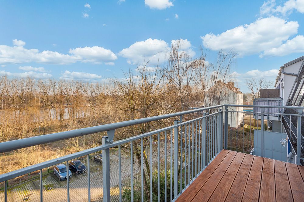 Balkon mit Holzboden und Metallgeländer, Blick auf Bäume und parkende Autos.