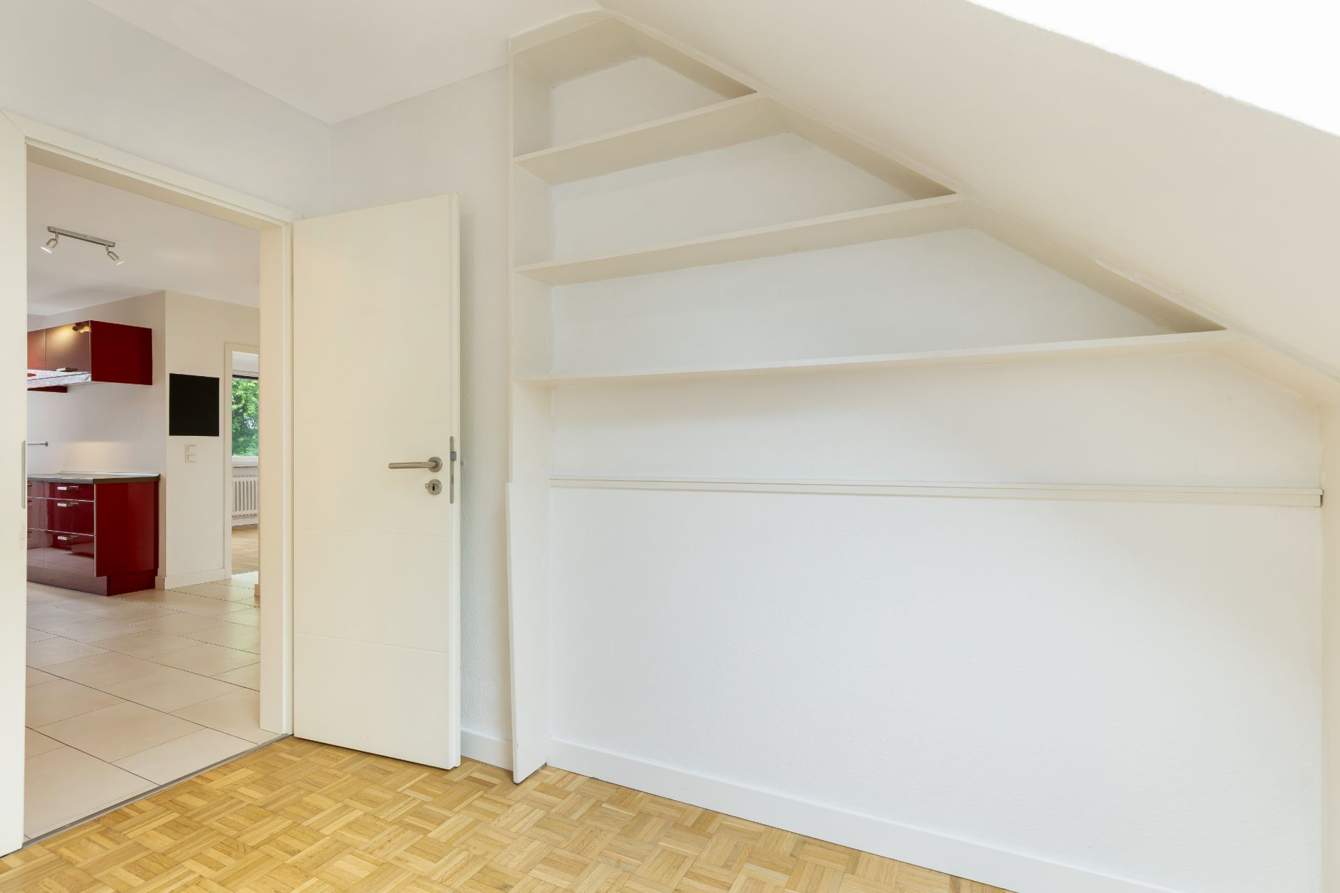 Zimmer mit Parkettboden, weißen Wänden und offenen Regalen unter einer Dachschräge.